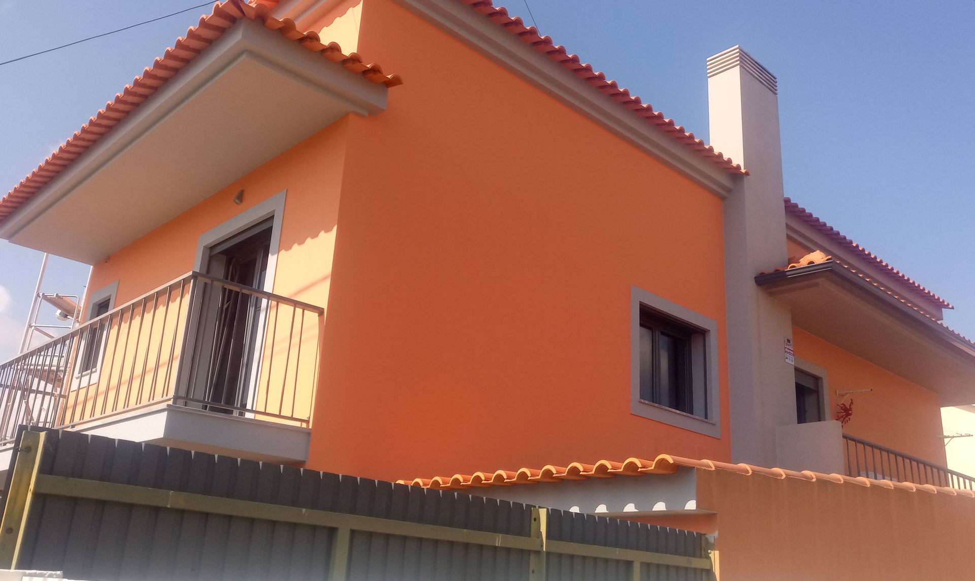 Casa laranja de dois andares com varanda e chaminé sob um céu azul claro.