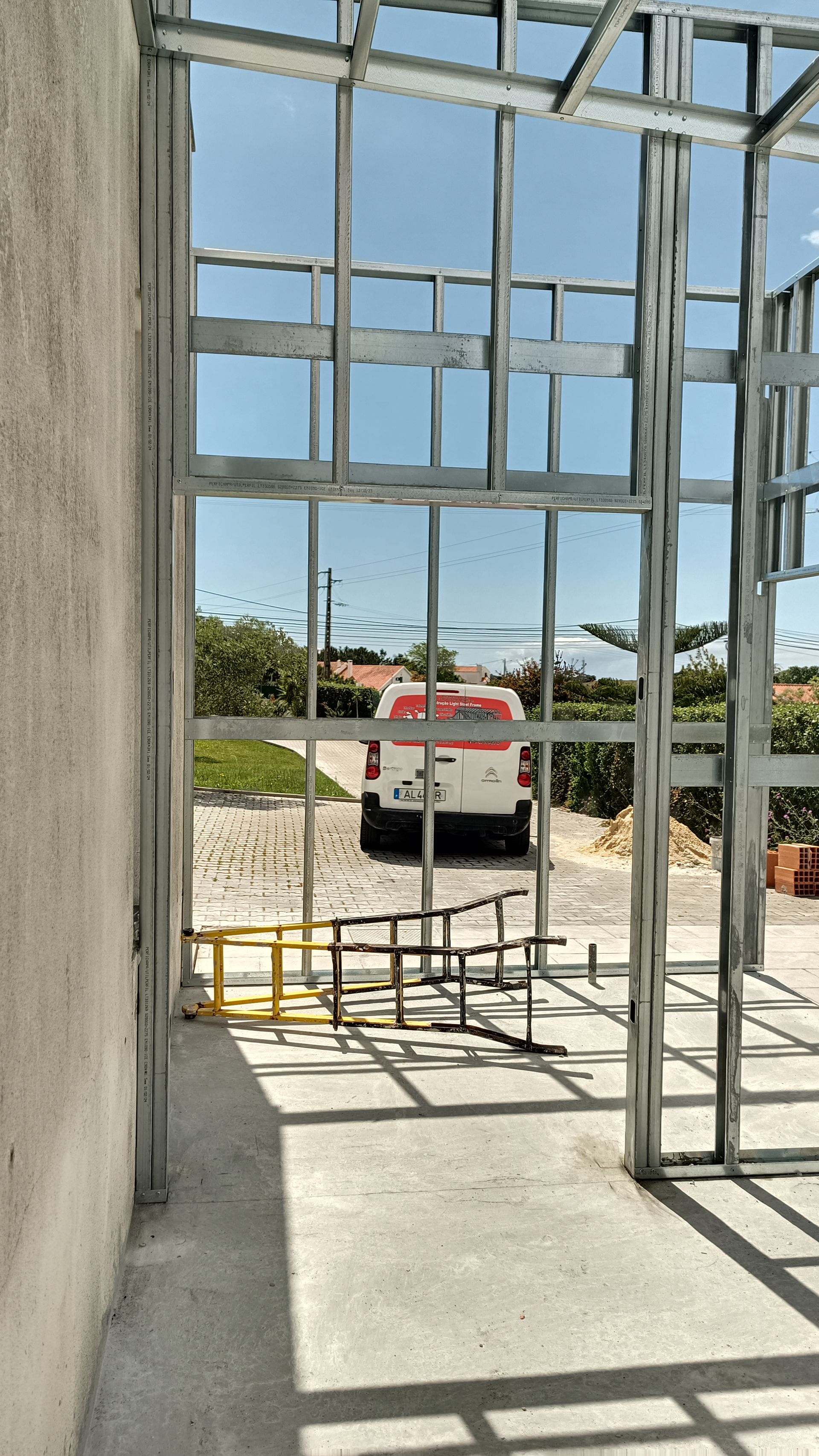 Estrutura metálica de um edifício em construção, com vista para um caminhão branco e céu azul claro.