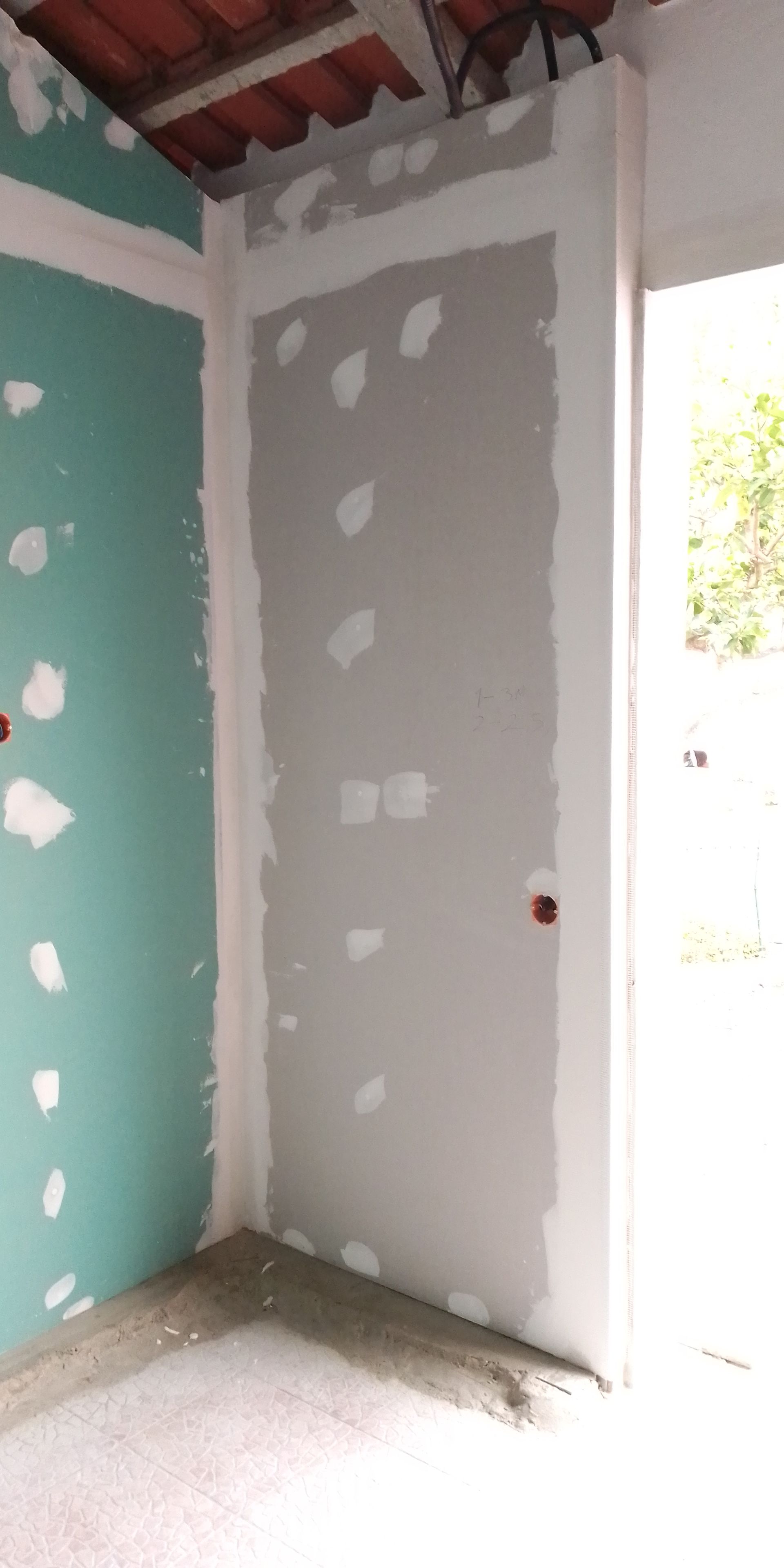 Interior de um cômodo em construção, com trabalhos de drywall e gesso em andamento.