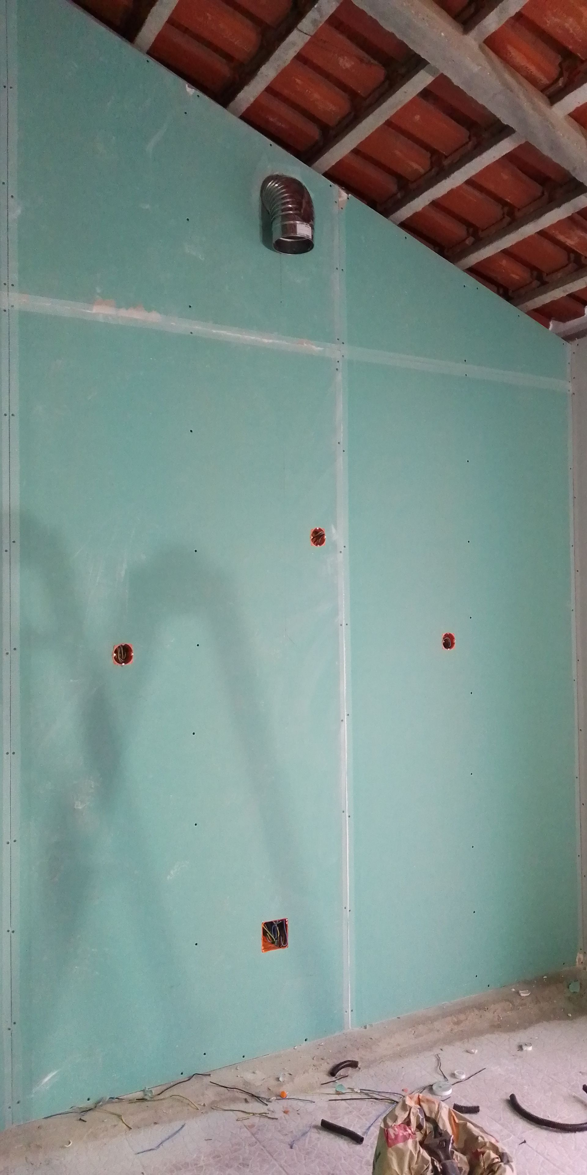 Parede interna com drywall azul-petróleo e caixas elétricas aparentes. Teto com telhas vermelhas aparentes.
