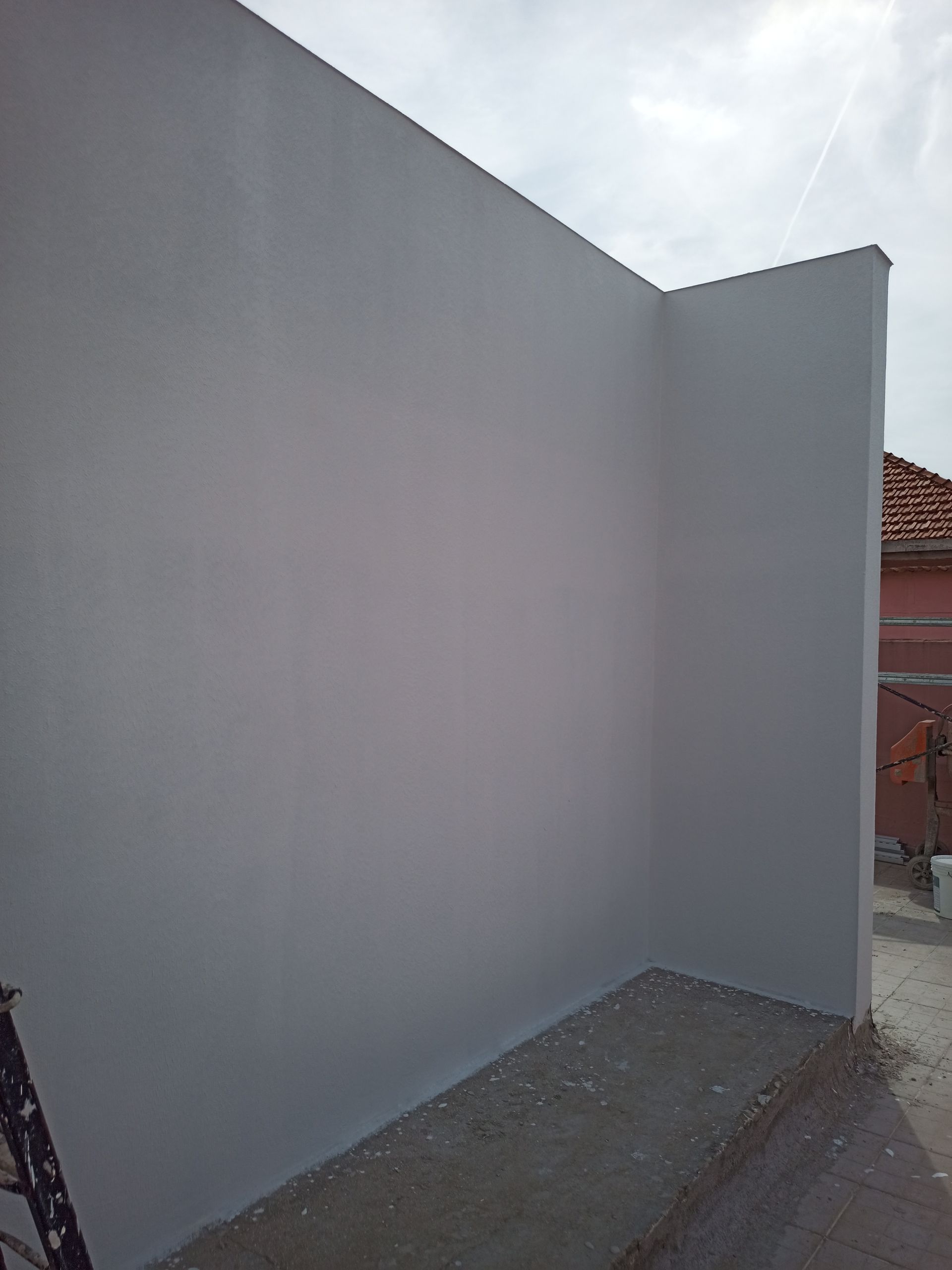 Canto de parede externa pintada de cinza, céu nublado ao fundo.