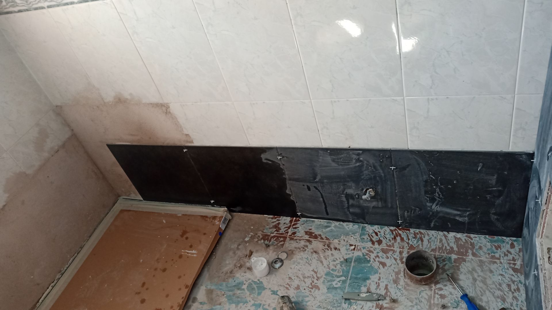 Banheiro em reforma com azulejos escuros na parede e entulho no chão.