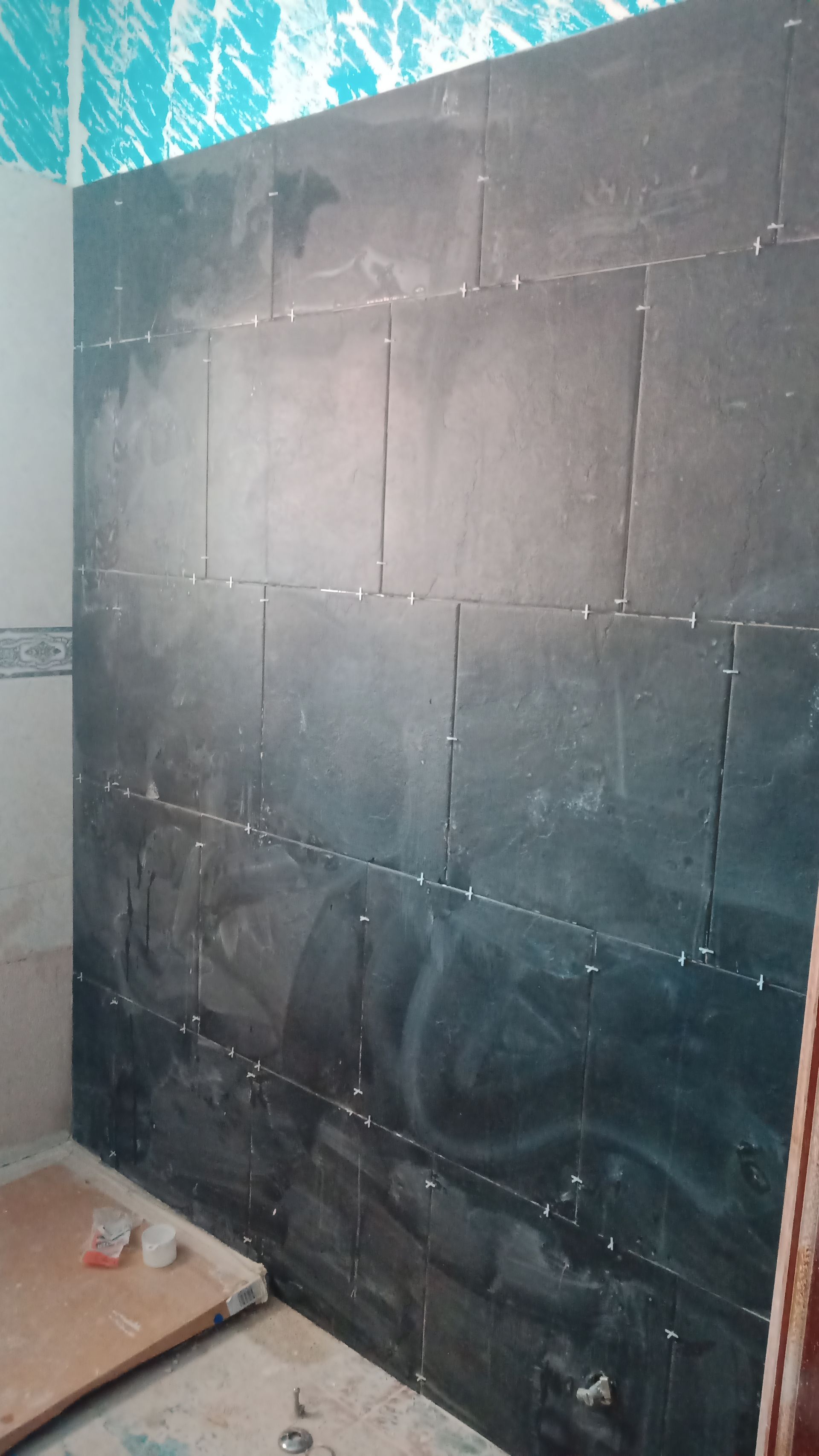 Parede do chuveiro revestida com azulejos pretos em construção, com rejunte visível entre os azulejos.