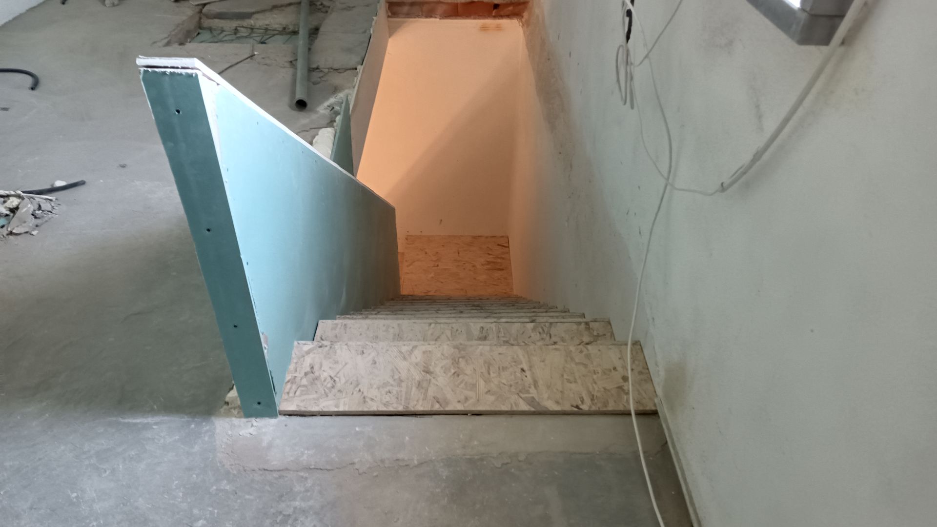 Escada em construção, com drywall e degraus inacabados que levam ao declive.