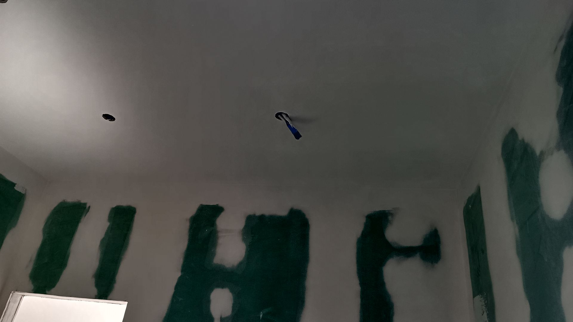 Quarto interior em construção, manchas verdes nas paredes, luzes no teto.