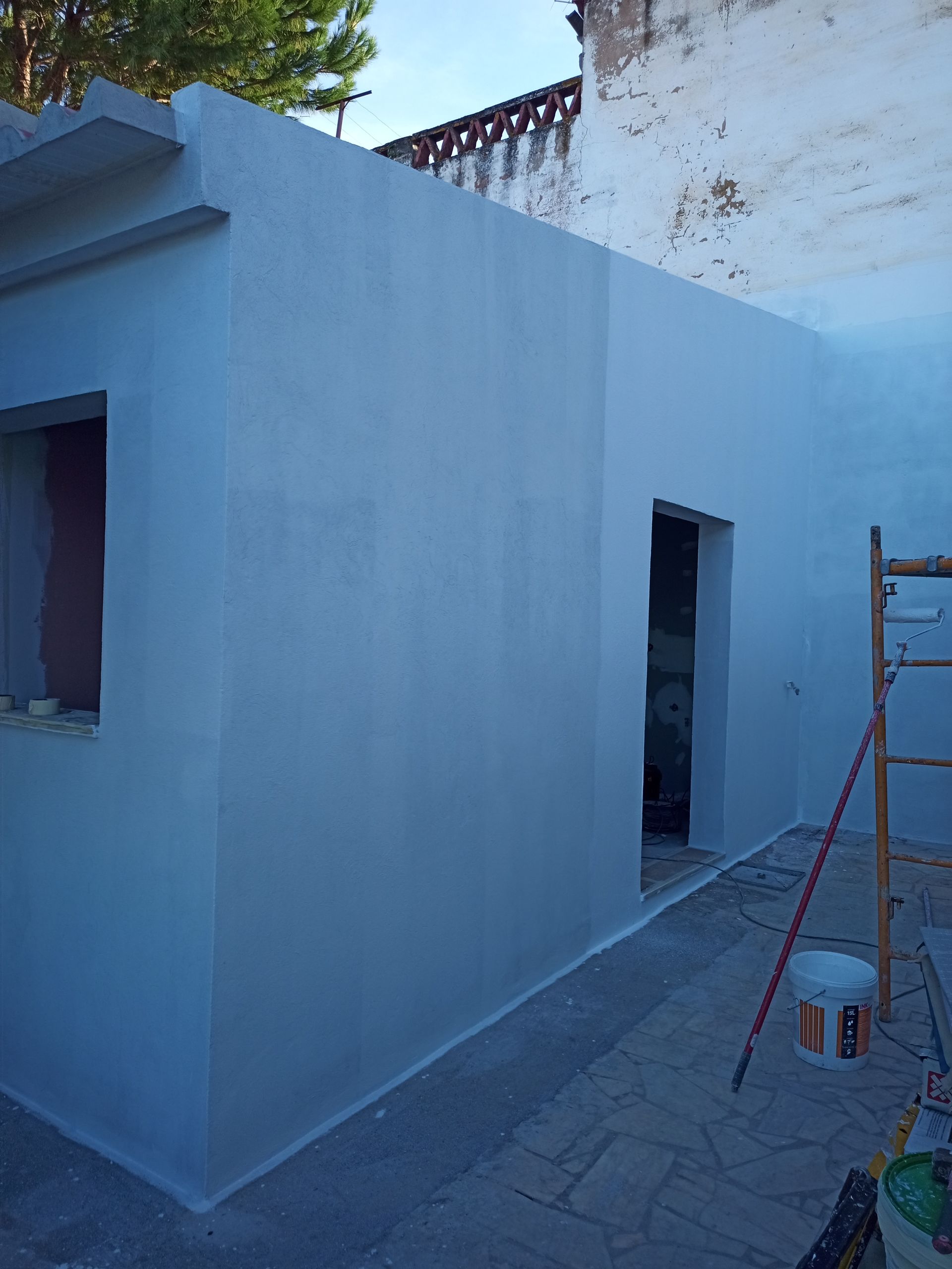 Exterior de um prédio em construção, recém-pintado de azul claro. Inclui porta aberta, janela e escada.
