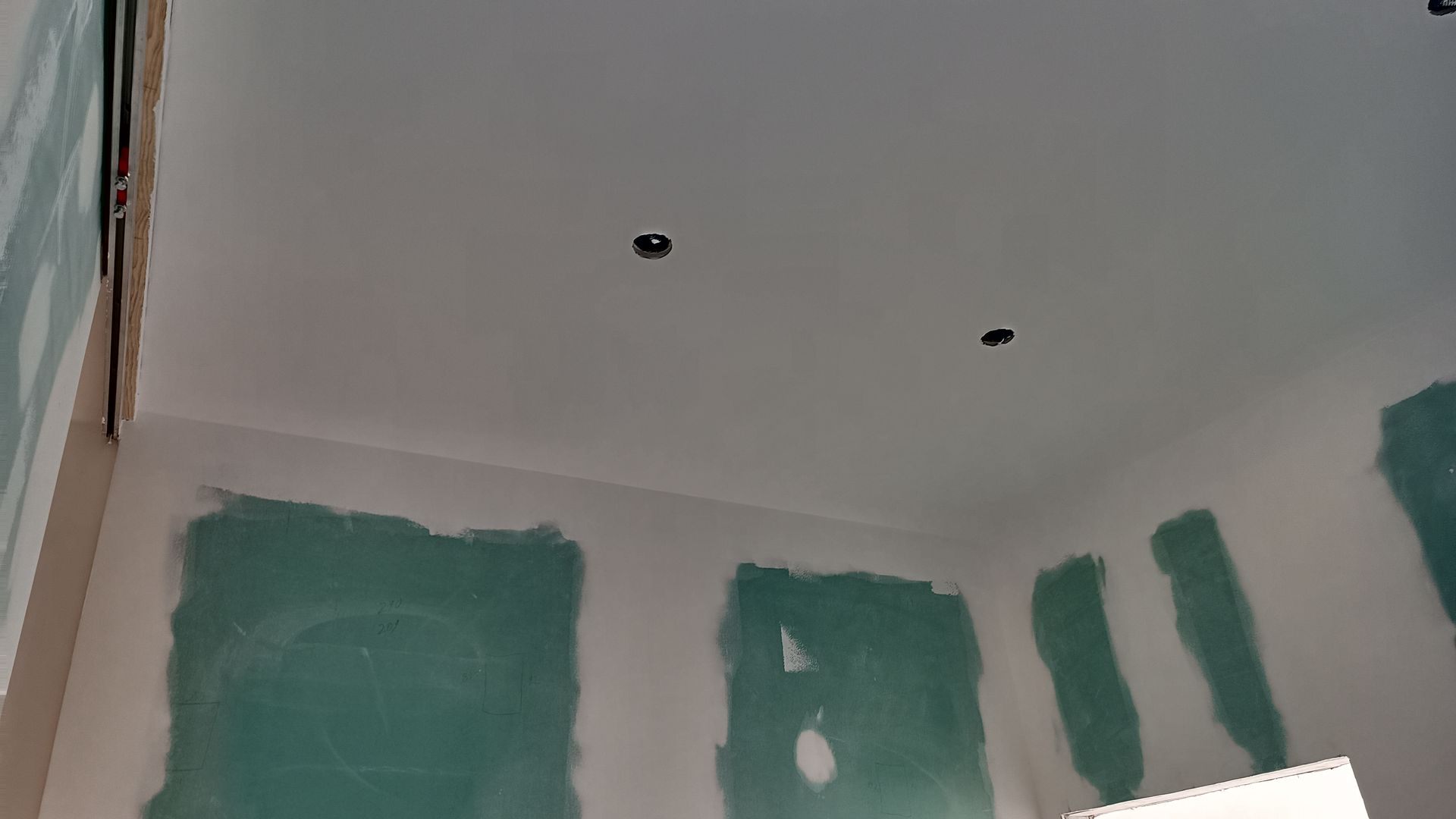 Ambiente interno em construção, com drywall verde, paredes brancas e luzes embutidas pretas no teto.