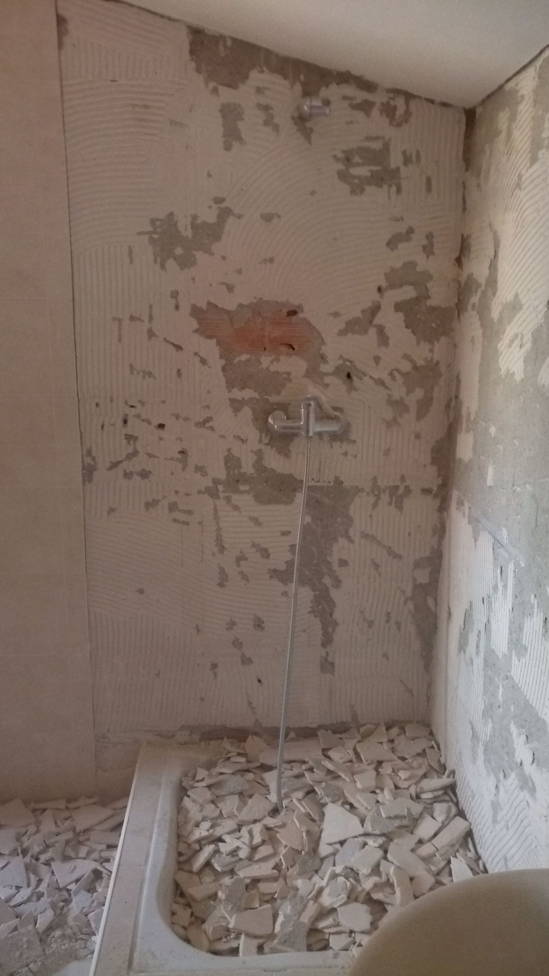 Banheiro em demolição: paredes arrancadas, restos de azulejos, encanamento exposto, banheira à vista.