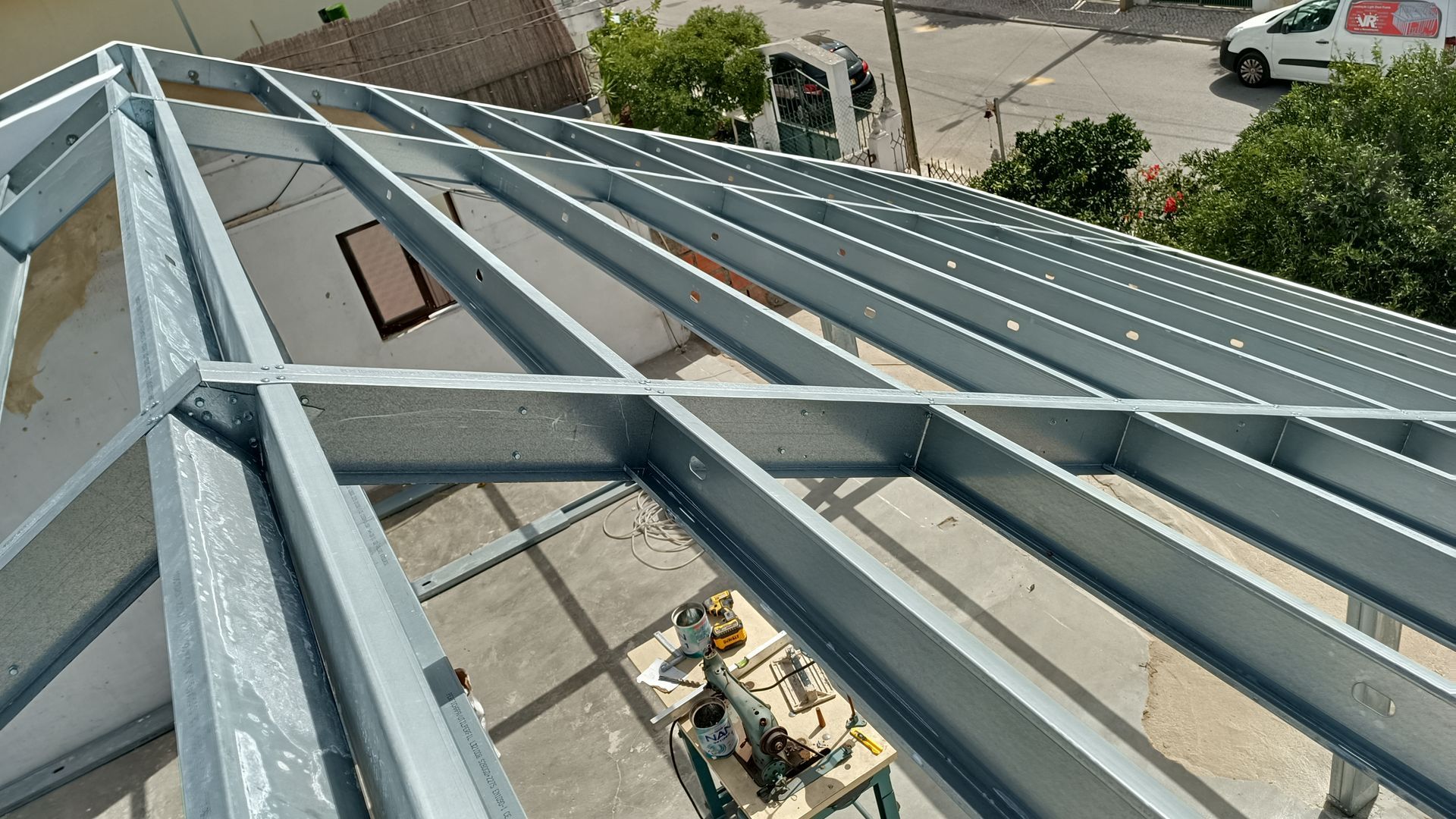 Estrutura metálica do telhado de um edifício em construção, com ferramentas visíveis por baixo.