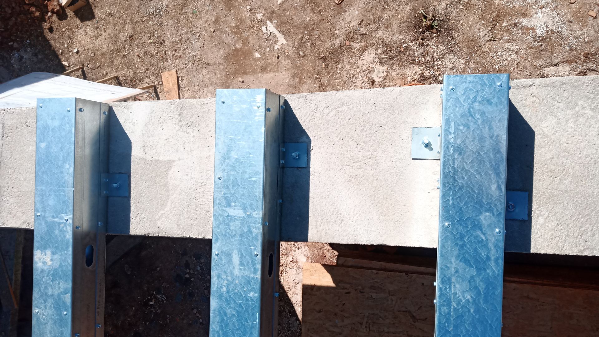 Postes de metal fixados em uma superfície de concreto, provavelmente para fins de construção, com solo marrom visível.