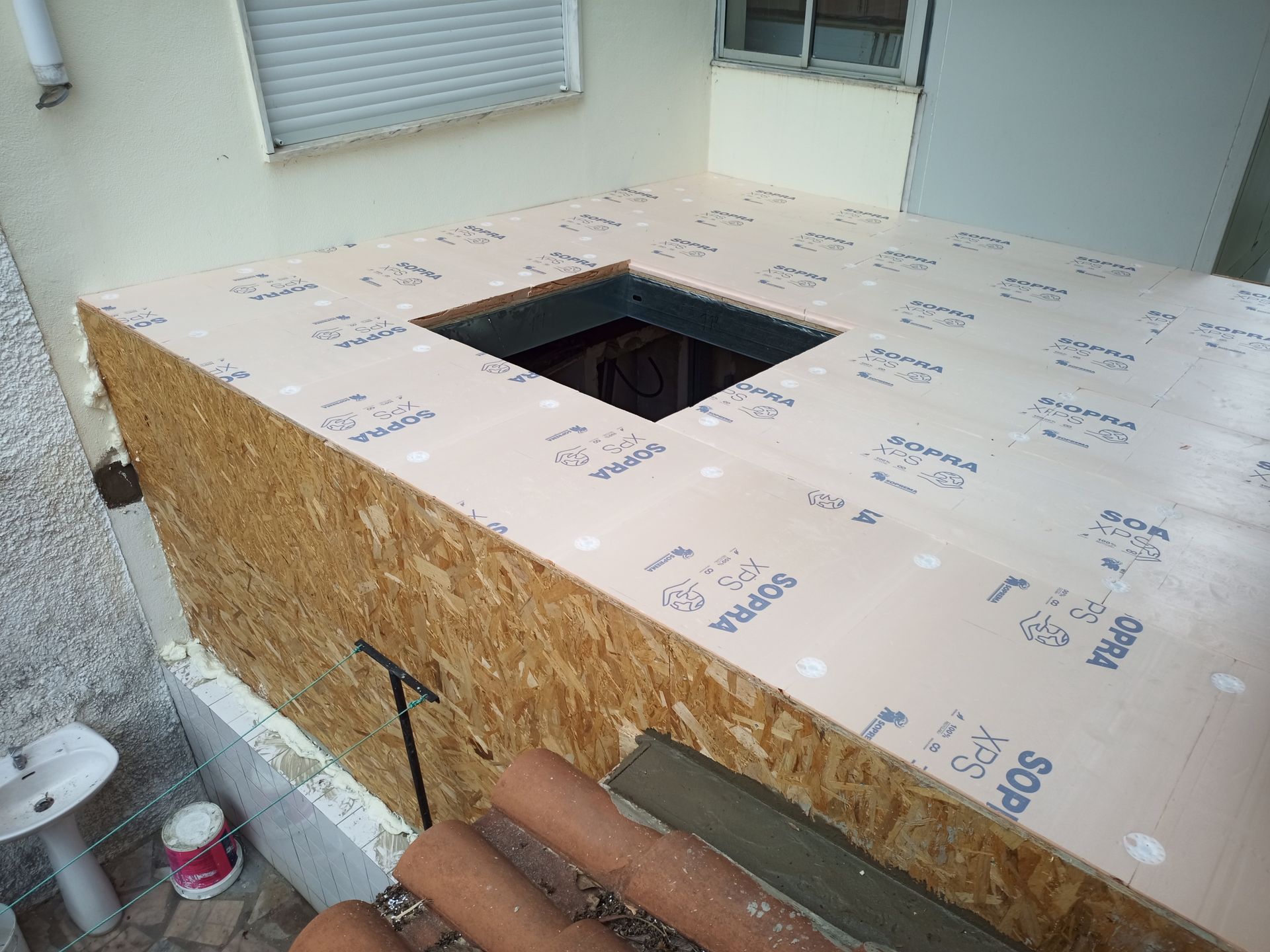 Construção de uma estrutura semelhante a um deck com um buraco quadrado, paredes de OSB e isolamento, encostada a um edifício.