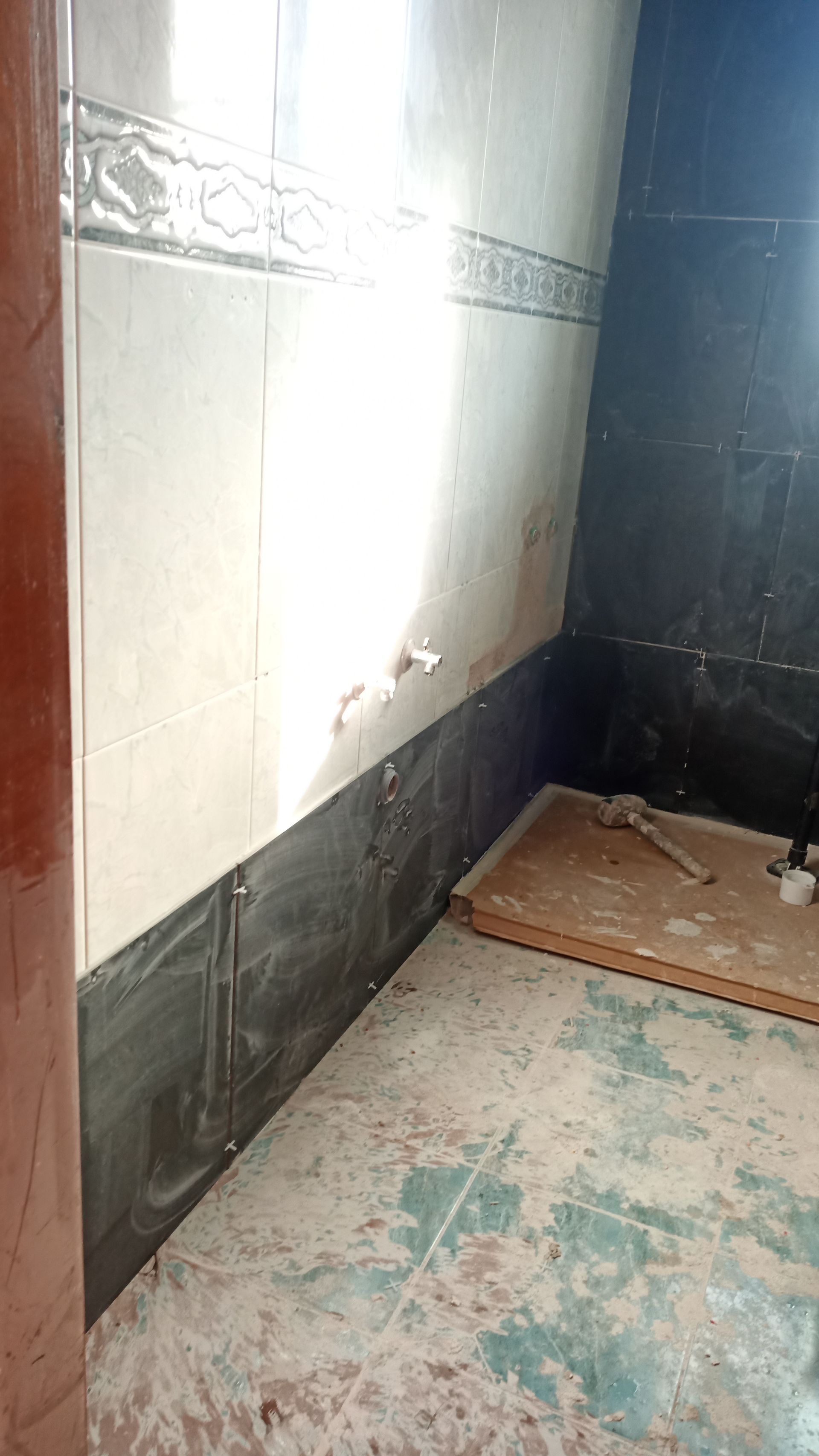 Banheiro com paredes e piso revestidos com azulejos, encanamento aparente, construção inacabada.