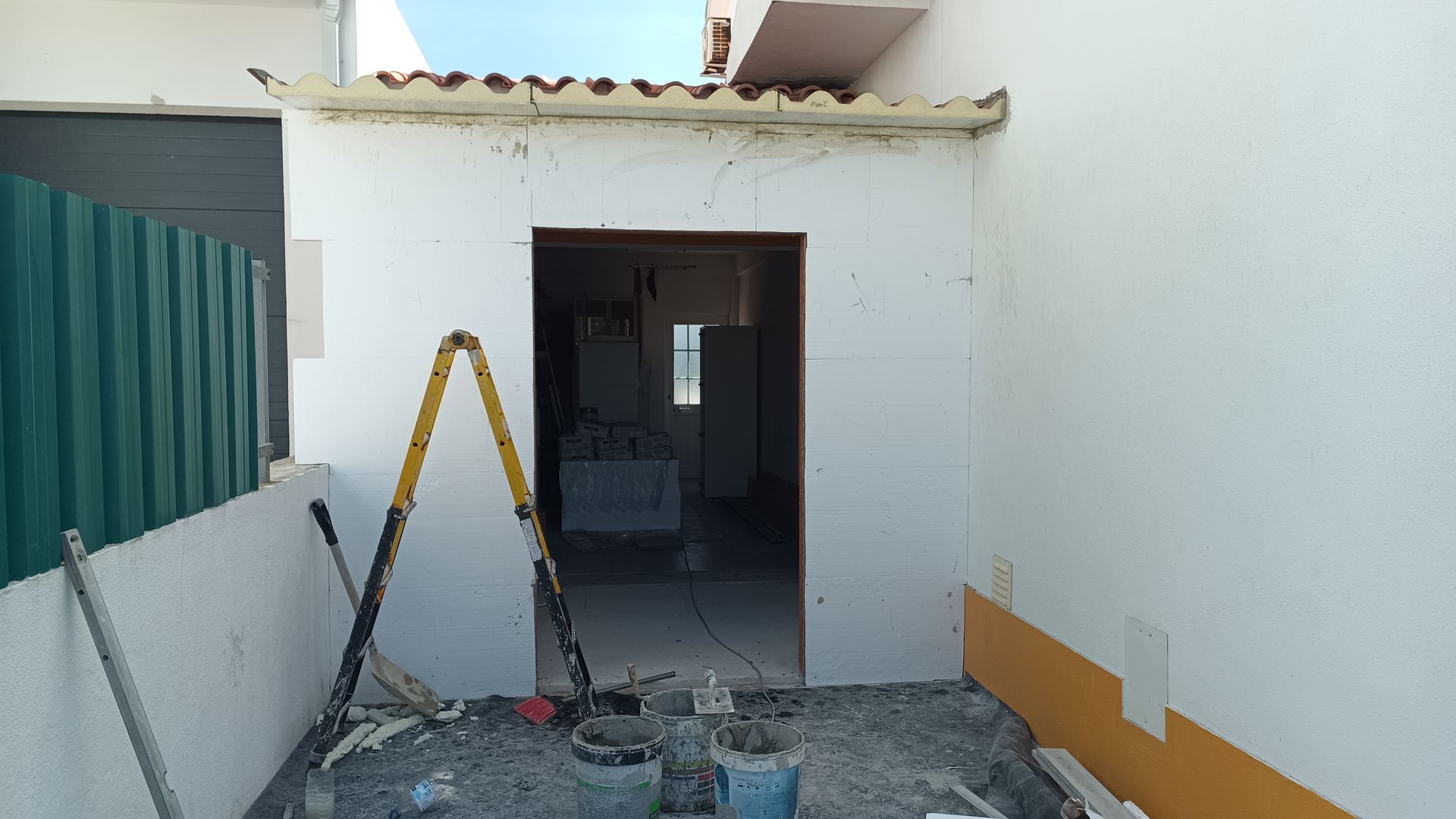 Exterior de um edifício em construção, mostrando a porta de entrada, a escada e os entulhos da obra.