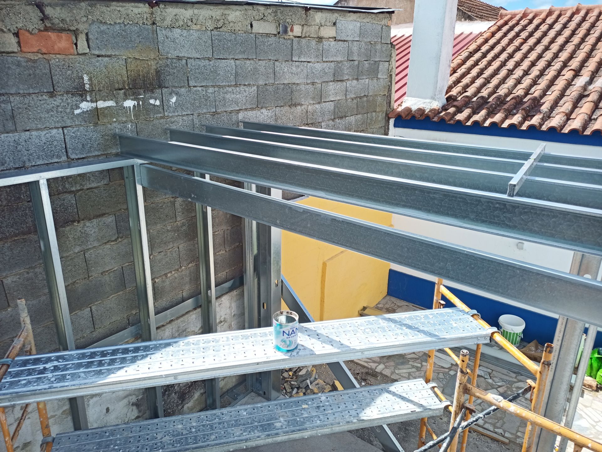 Construção de uma estrutura metálica para telhado, fixada a uma parede de blocos de concreto, com andaimes.