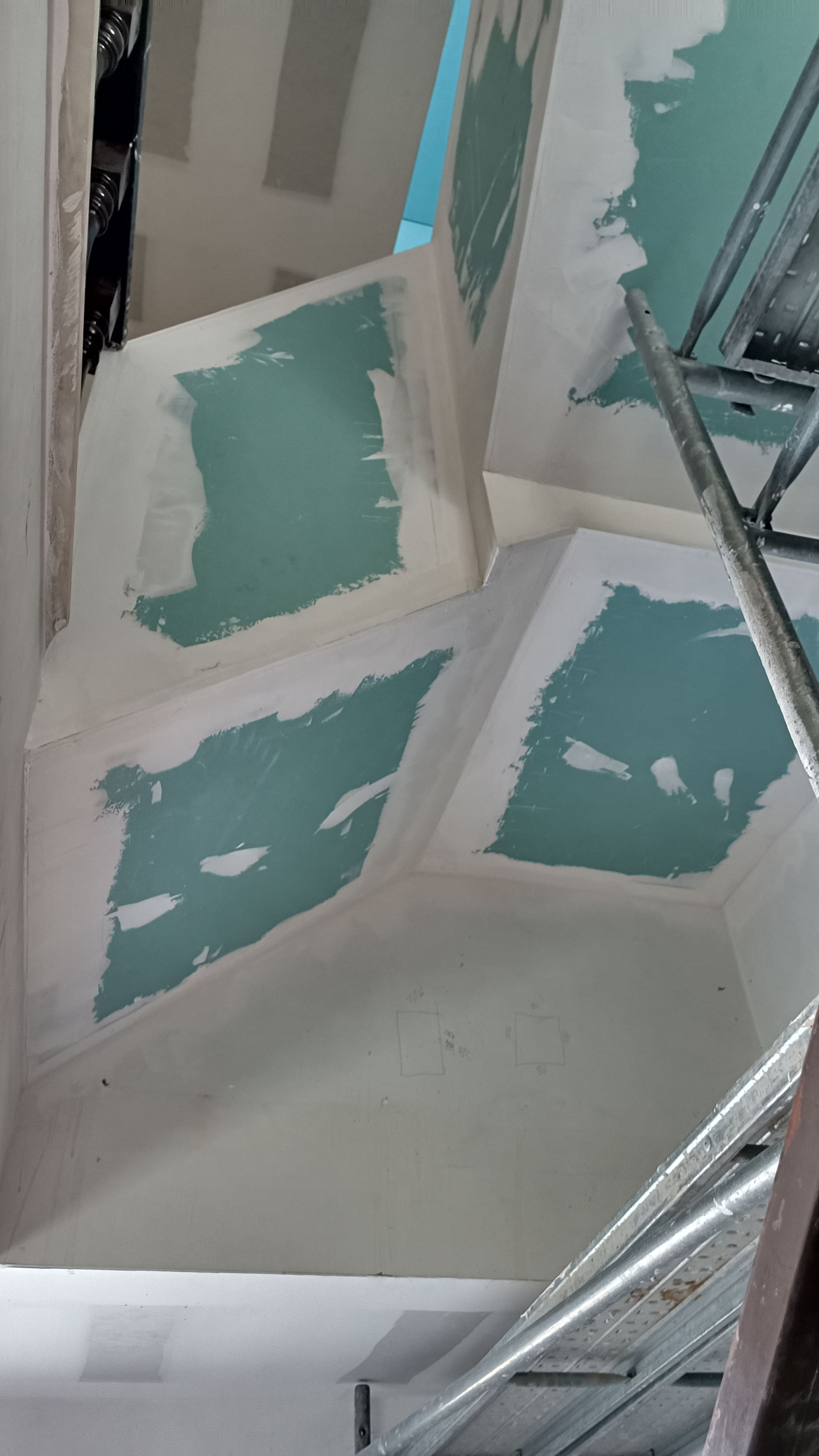 Teto com drywall parcialmente acabado e massa corrida. Paredes em azul claro visíveis. Andaime à direita.