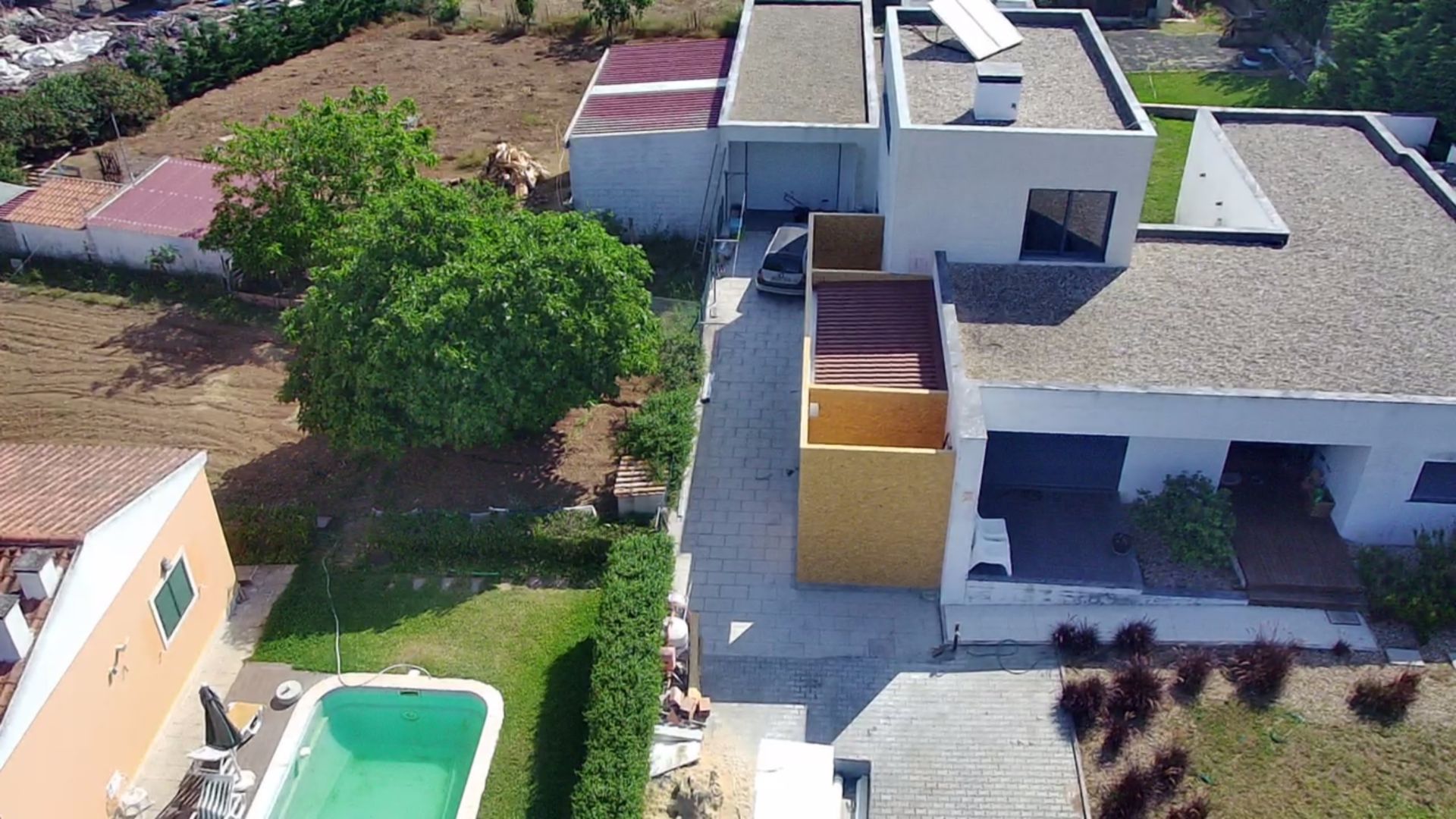 Vista aérea de um complexo de casas modernas com piscina, gramado e uma longa entrada para carros.