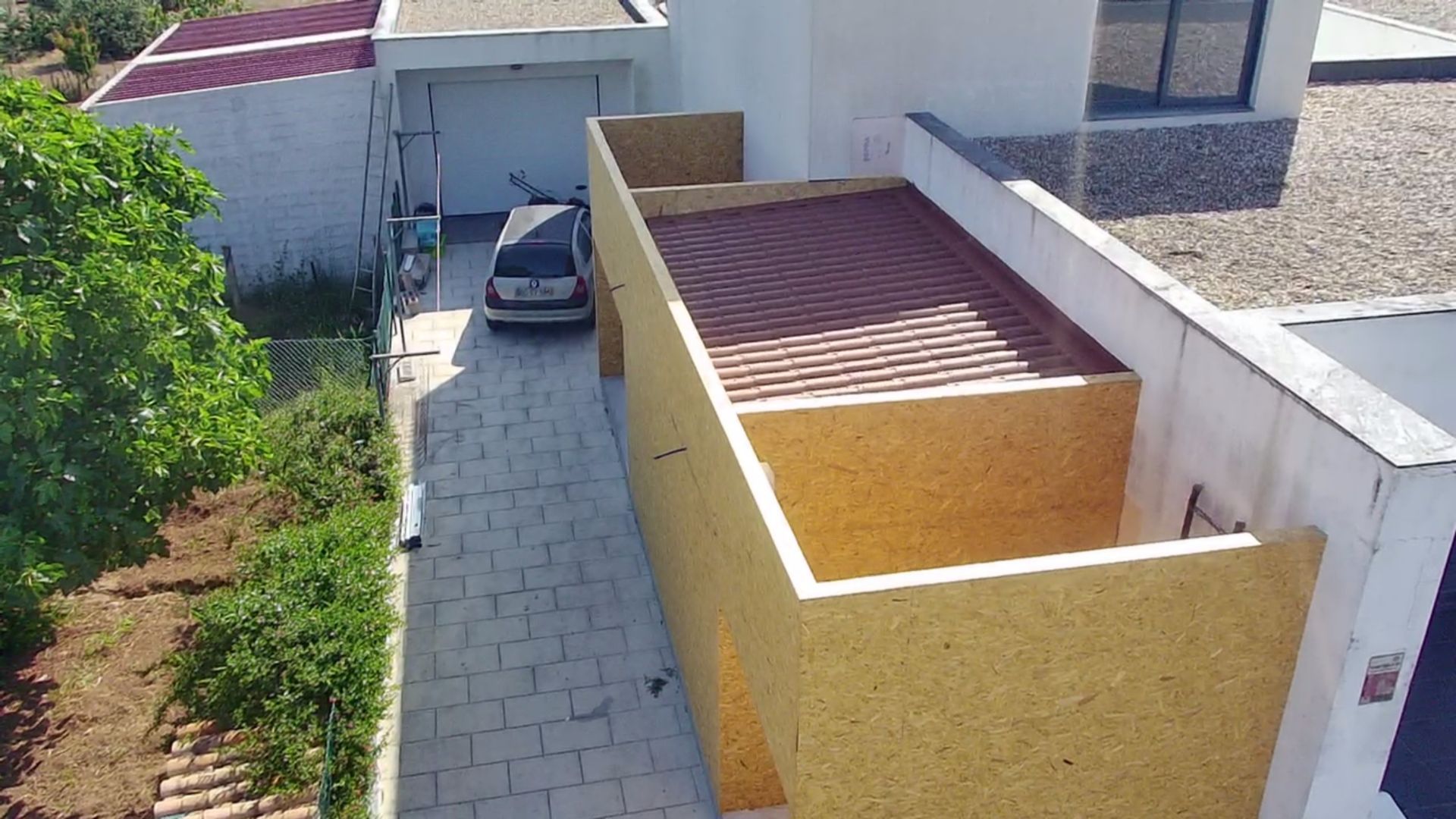 Entrada de garagem com carro estacionado ao lado de uma estrutura de paredes amarelas e telhado marrom.