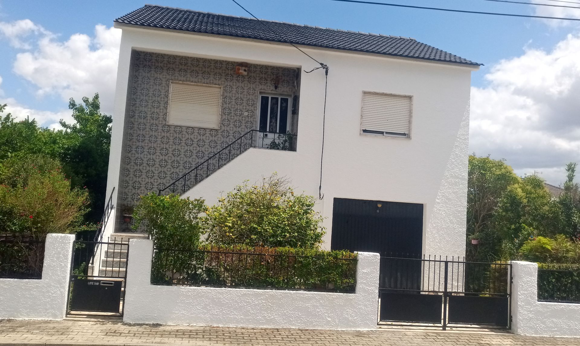Casa branca de dois andares com telhado e porta da garagem pretos. Fachada de pedra no segundo andar. Cerca preta na frente.