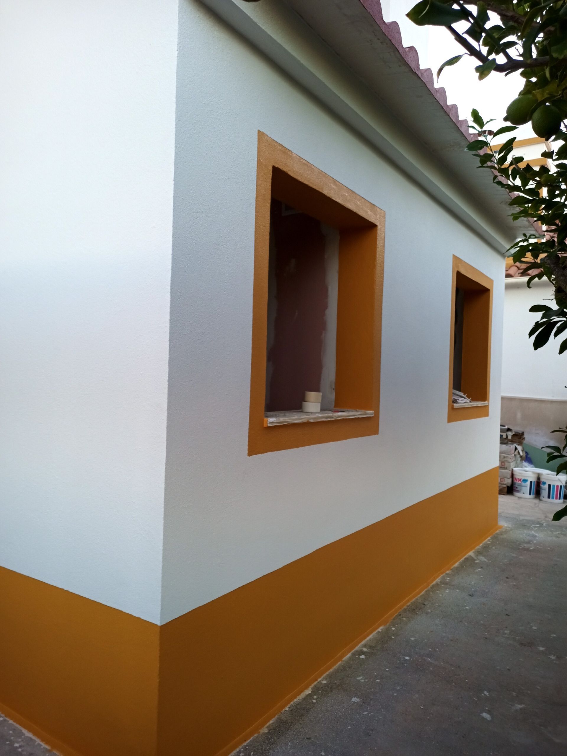 Exterior de um edifício pintado de branco e ocre, com duas molduras de janela.