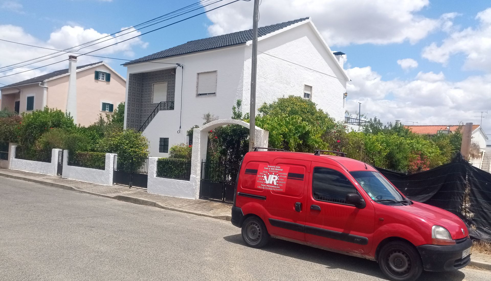 Casa branca com uma carrinha vermelha estacionada na rua em frente a uma sebe.