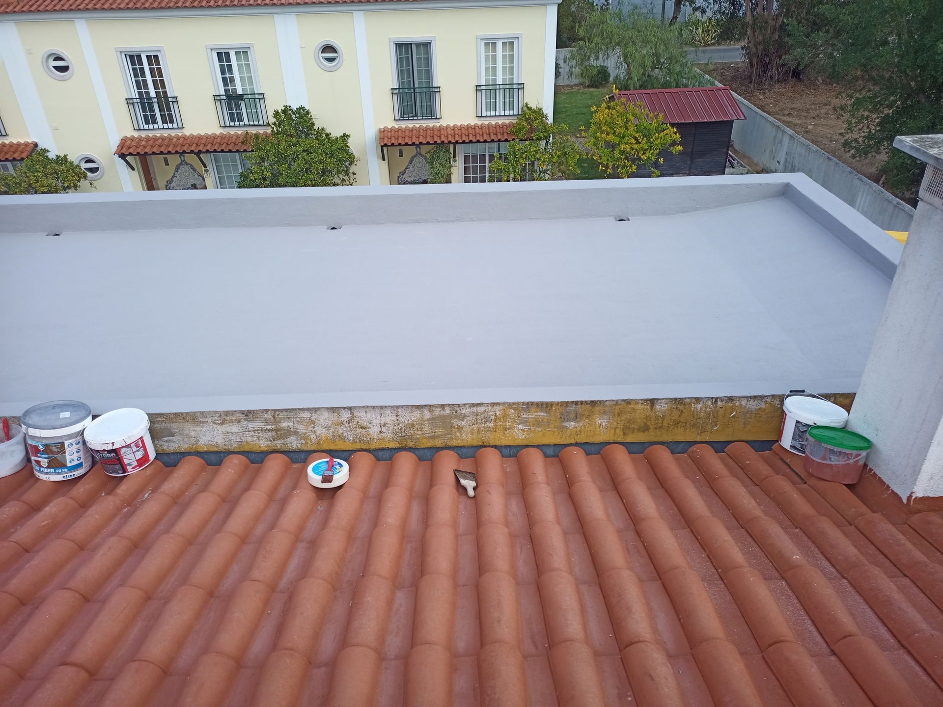 Um telhado plano pintado de cinza ao lado de um antigo telhado de telhas vermelhas, com um prédio ao fundo.