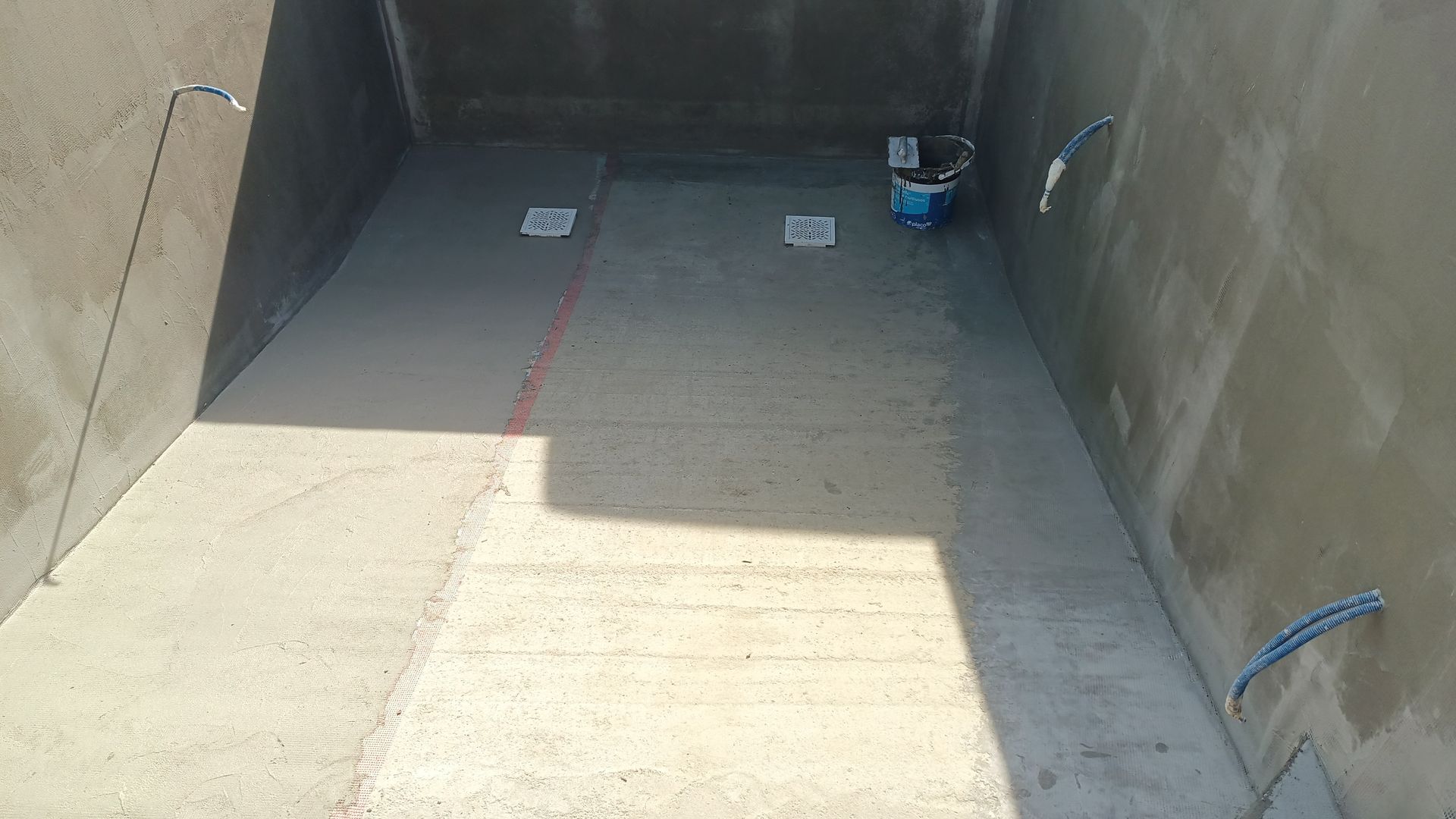 Sala de concreto em construção; paredes e piso nus com fiação exposta.