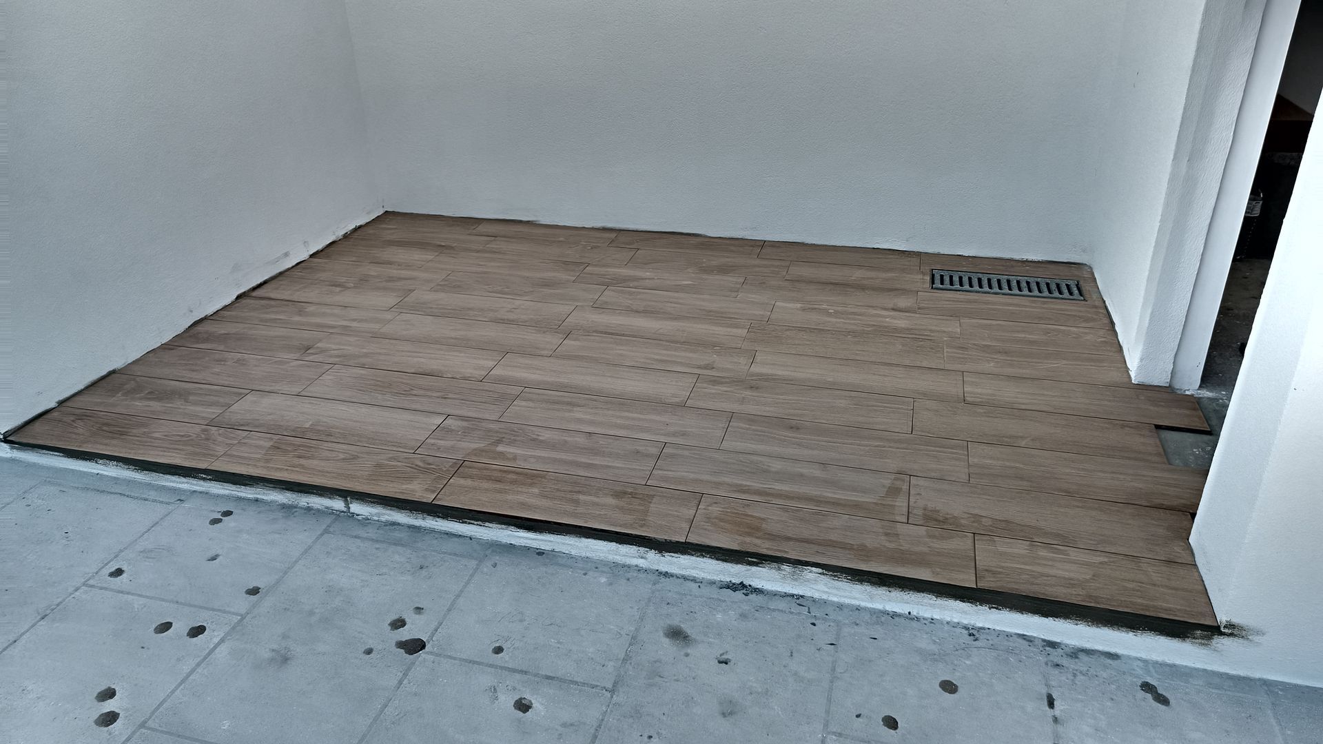 Um cômodo com piso que imita madeira assentado sobre uma base de concreto. Um ralo é visível.