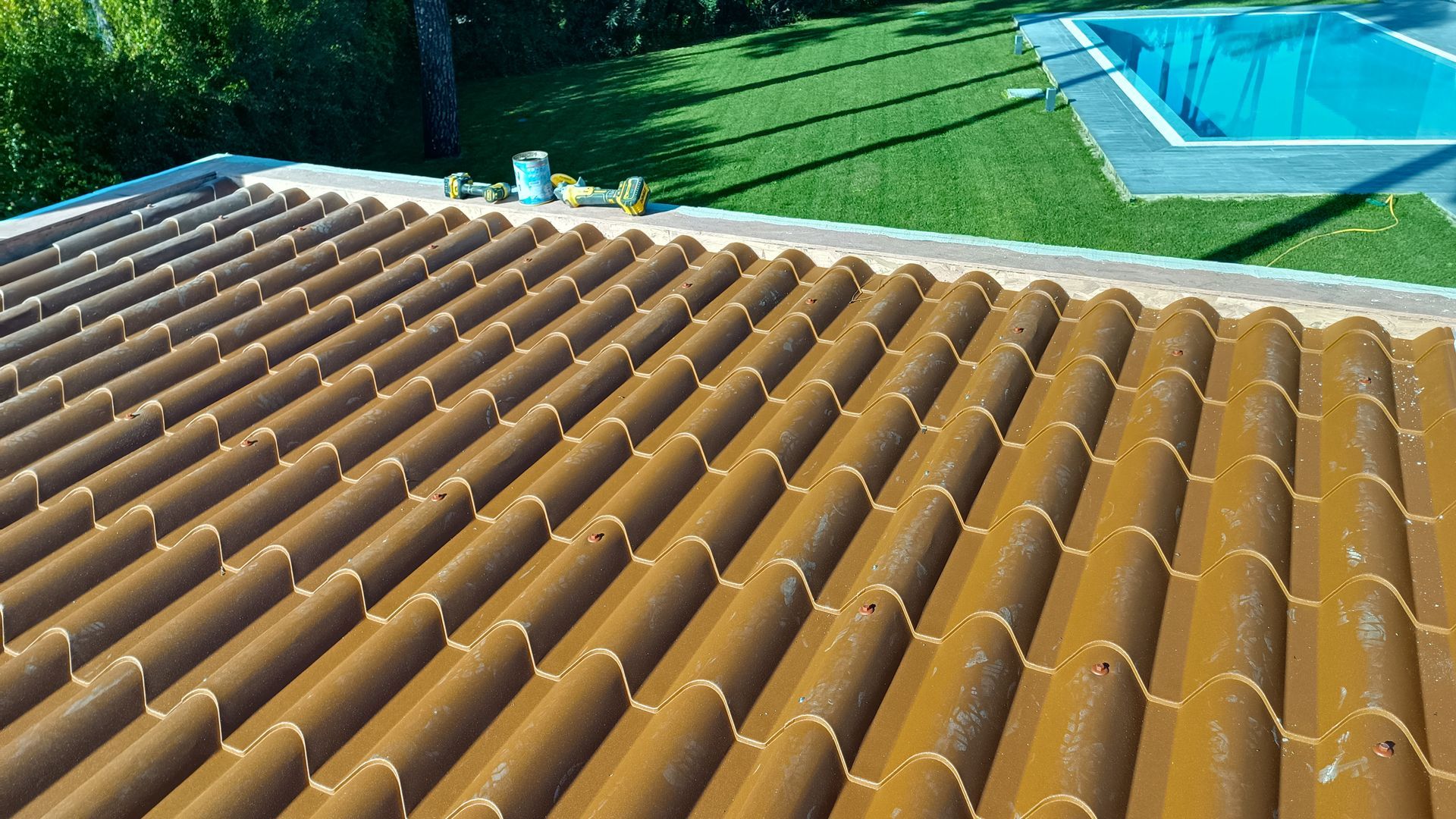 Telhas cerâmicas marrons sob a luz do sol, com piscina e gramado ao fundo.