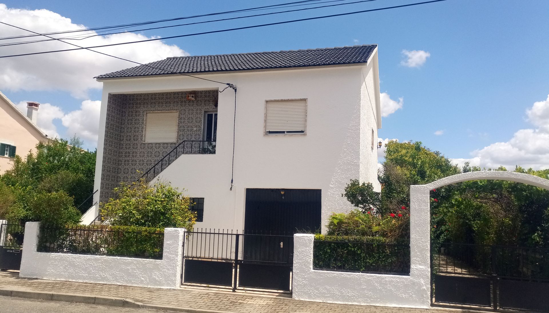 Casa branca de dois andares com telhado preto e garagem. Possui uma seção externa de tijolos.
