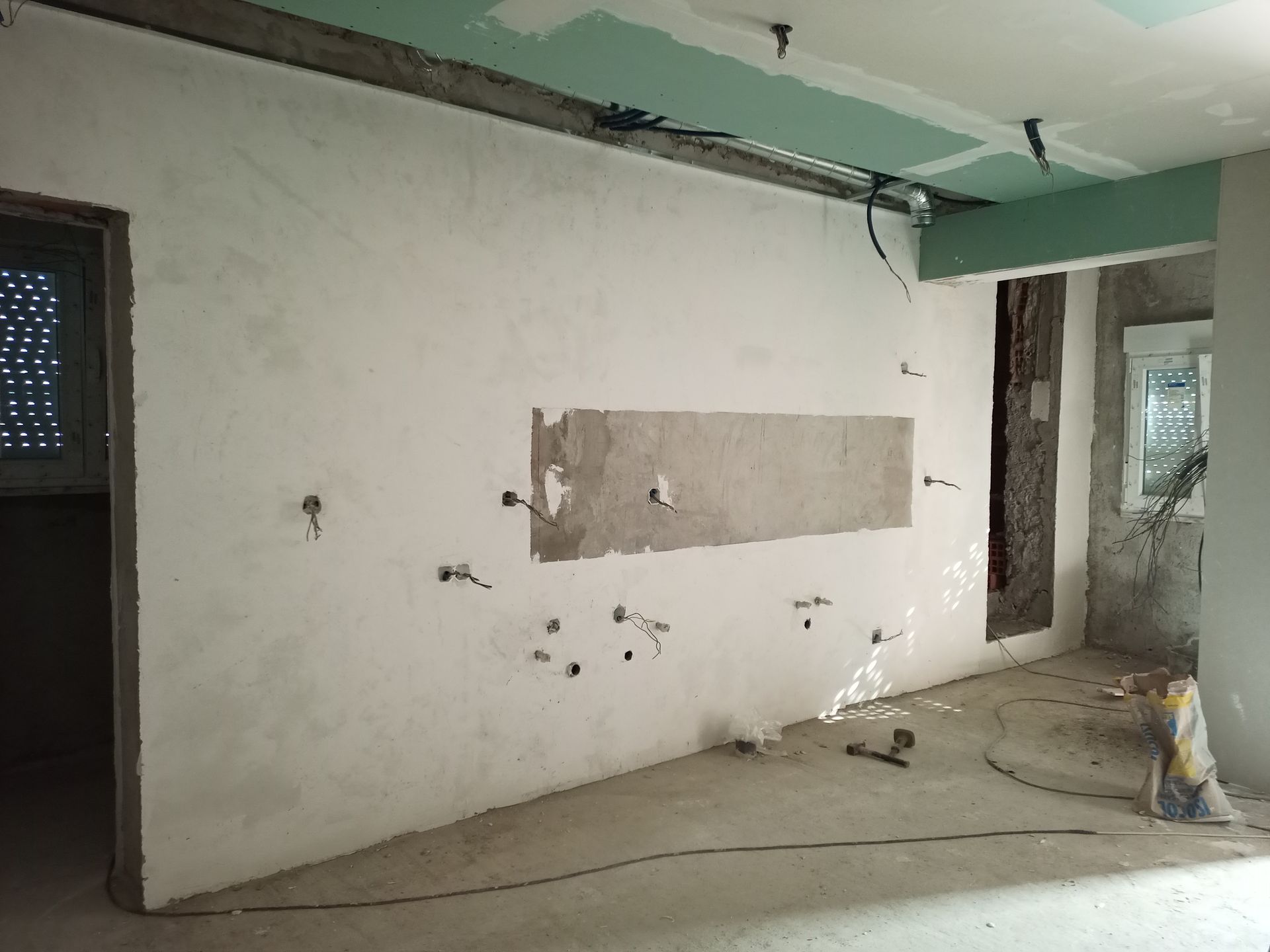 Interior de uma sala em construção, com fiação exposta, paredes inacabadas e piso de concreto.