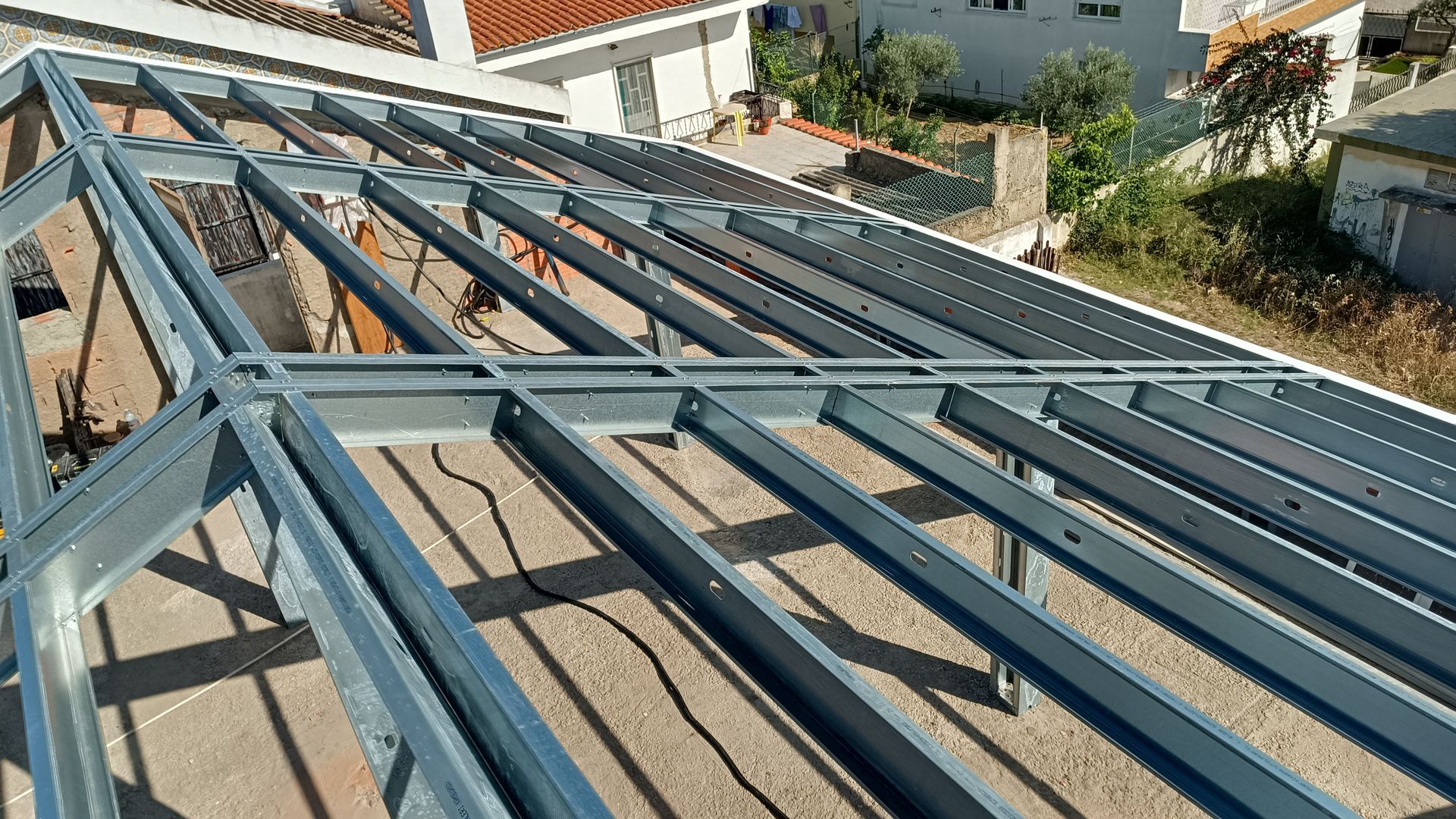 Estrutura metálica do telhado em construção em uma cobertura, com outros edifícios ao fundo.