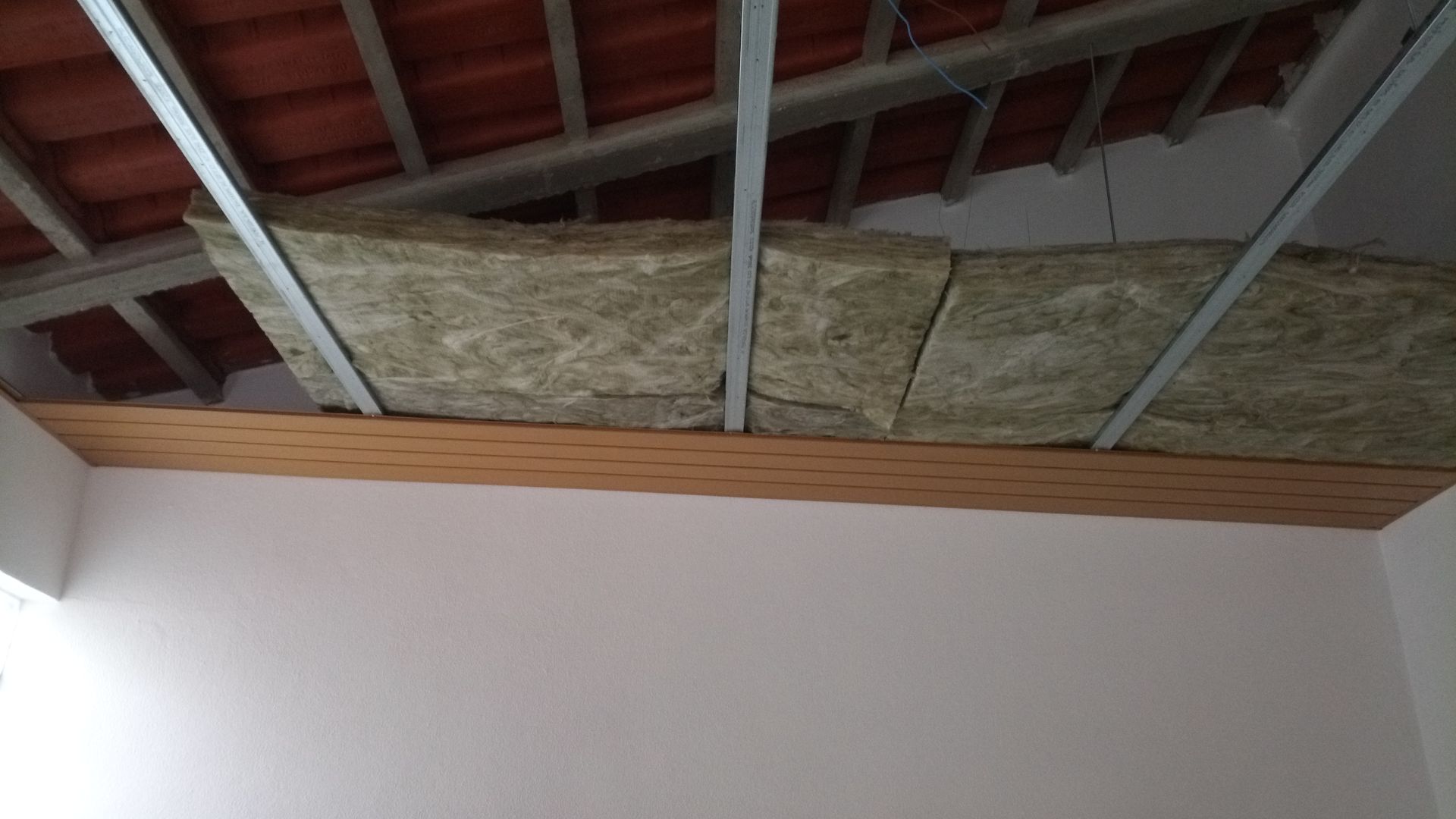 Isolamento e estrutura metálica instalados no teto, com telhas de terracota visíveis acima.