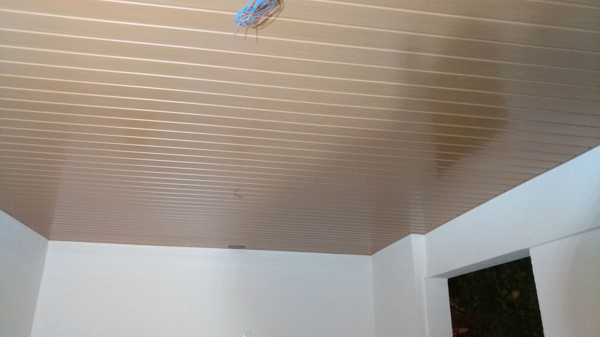Teto com painéis marrons em uma sala com paredes brancas. Fios elétricos pendem do teto.