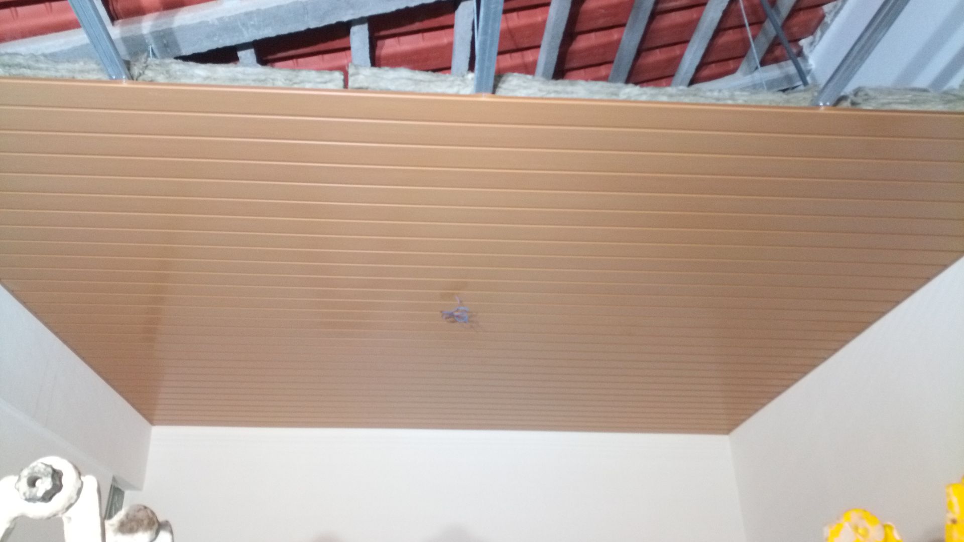 Teto de plástico marrom com estrutura metálica aparente acima, instalado em uma sala com paredes brancas.