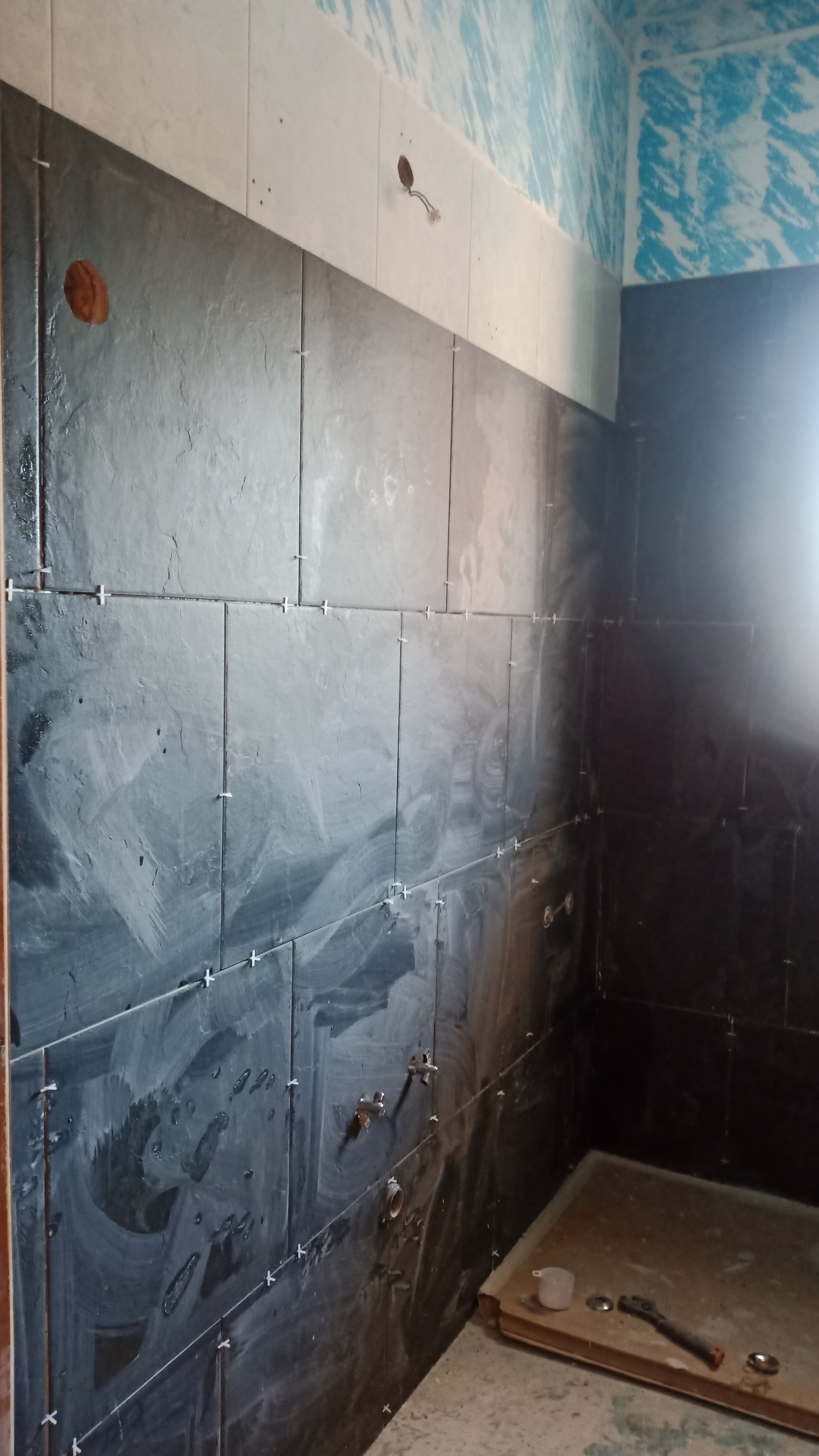 Parede do banheiro revestida com azulejos cinza-escuros em construção, com a área do chuveiro visível.