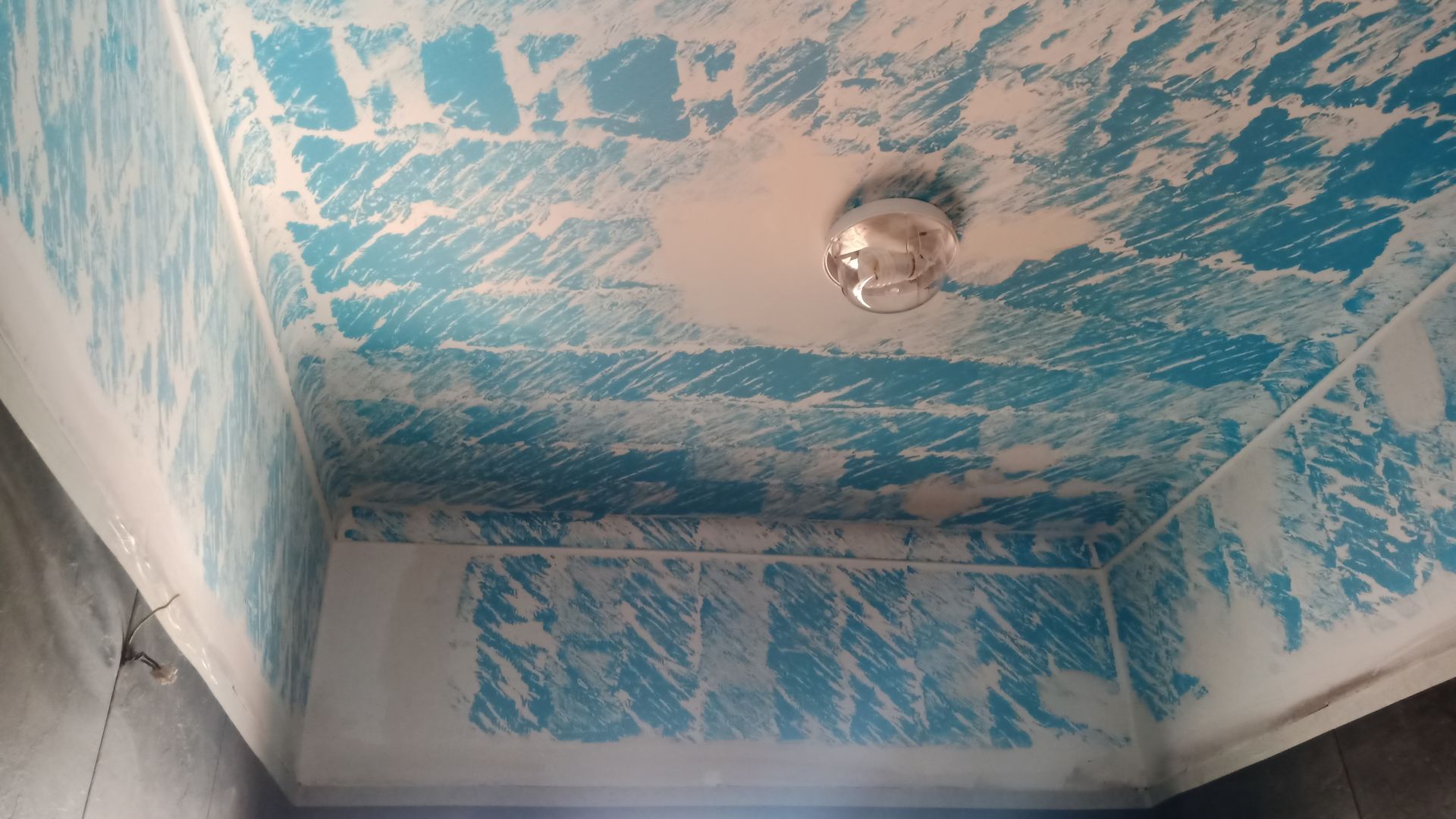 Teto azul com tinta descascando, luminária no centro.