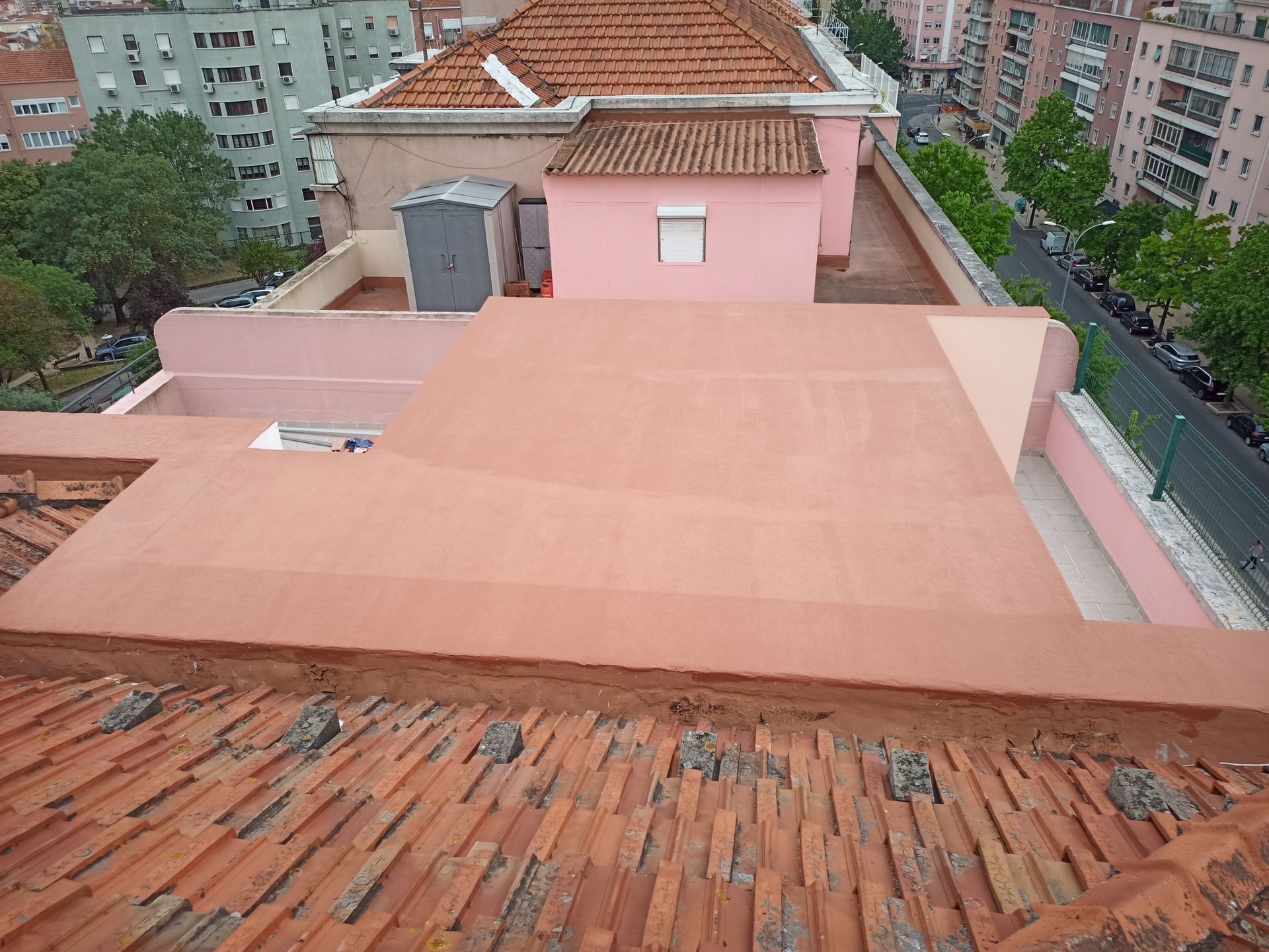 Vista do terraço com telhado de telha vermelha, seção rosa do edifício e prédios ao fundo.
