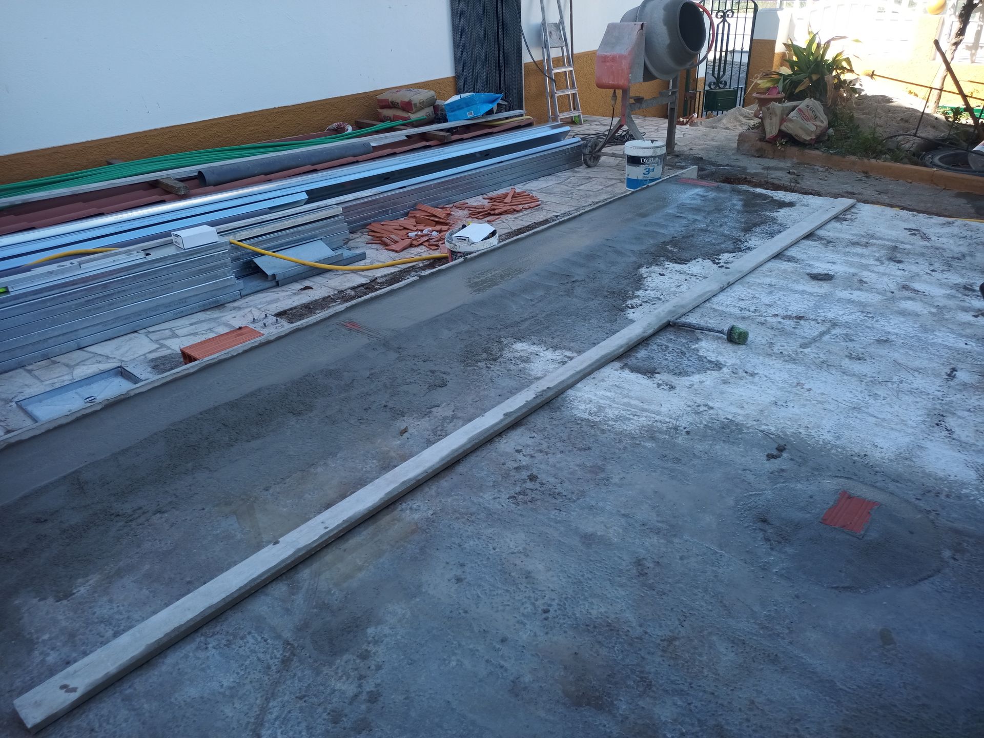 Obra de concreto em andamento: uma longa laje sobre cimento fresco, com materiais de construção ao fundo.