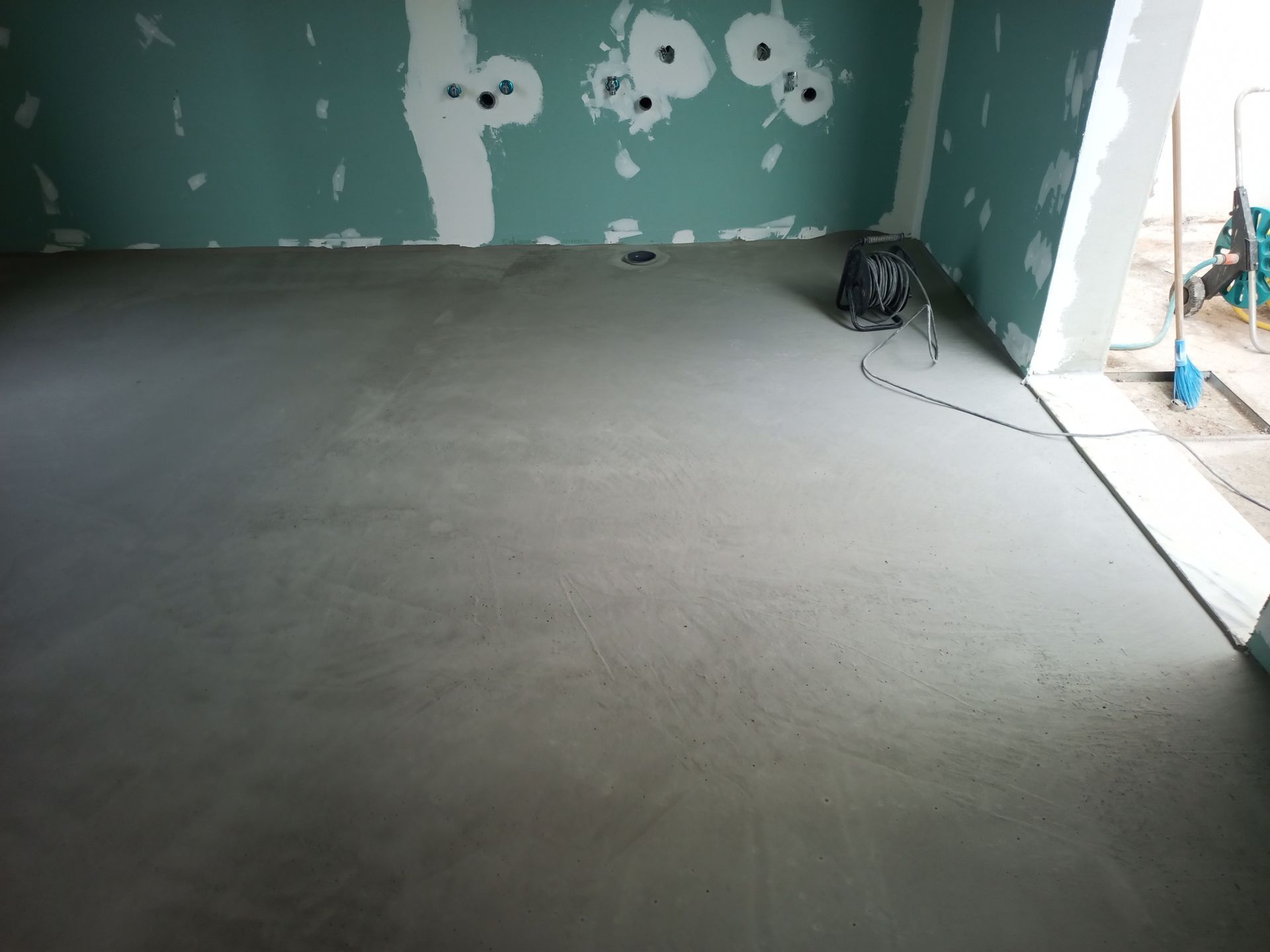 Piso de concreto cinza em uma sala com paredes verde-claras inacabadas.