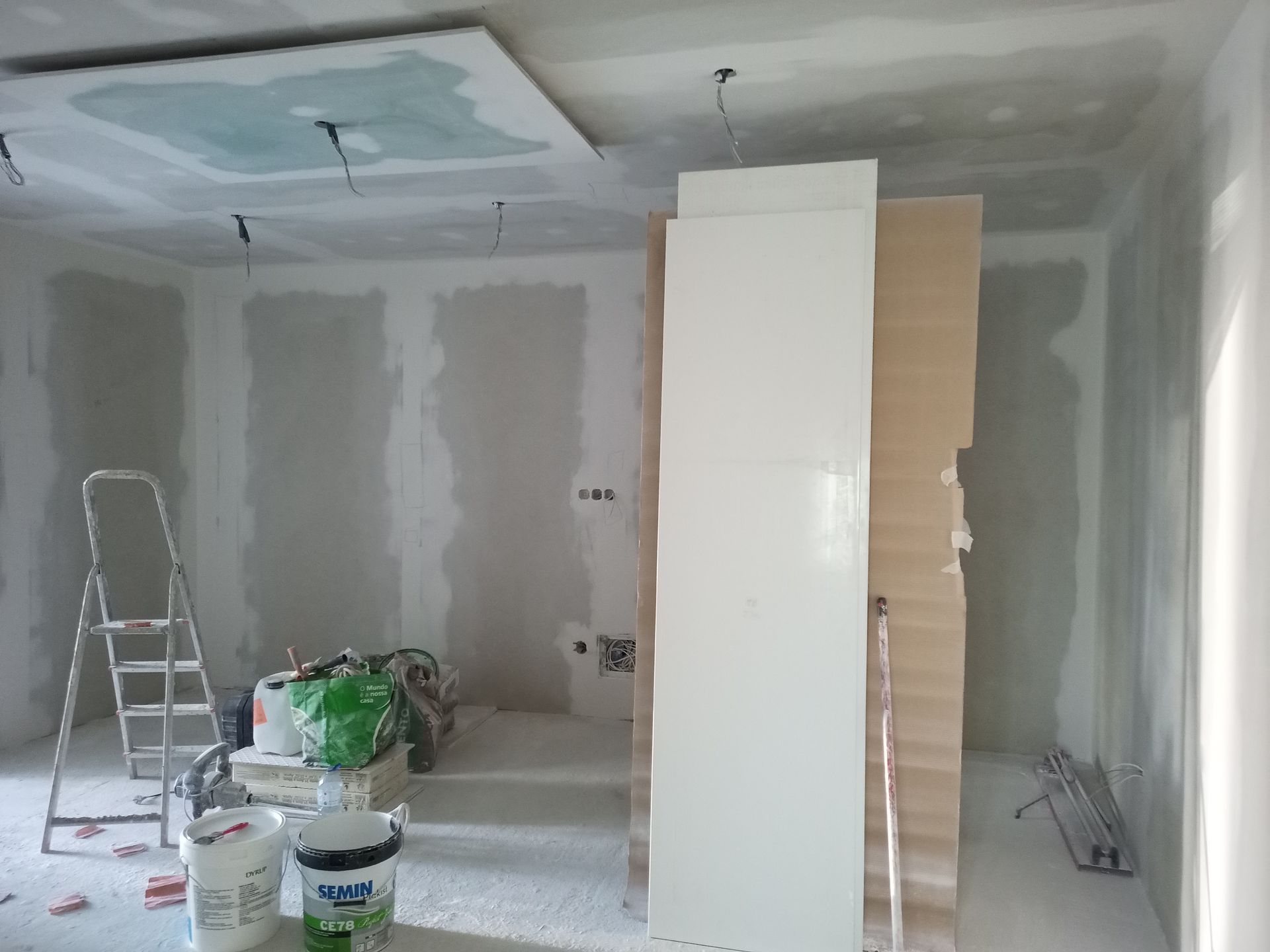 Sala em construção com drywall, ferramentas e materiais.