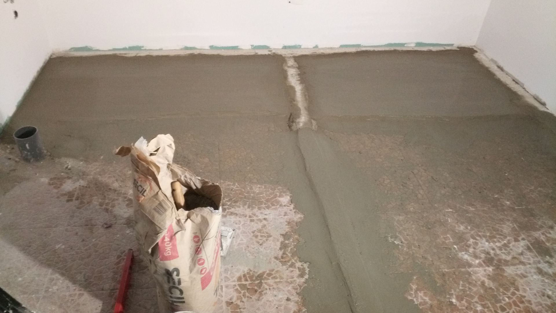 Sala com piso de concreto recém-colocado, com um saco de cimento aberto em primeiro plano.