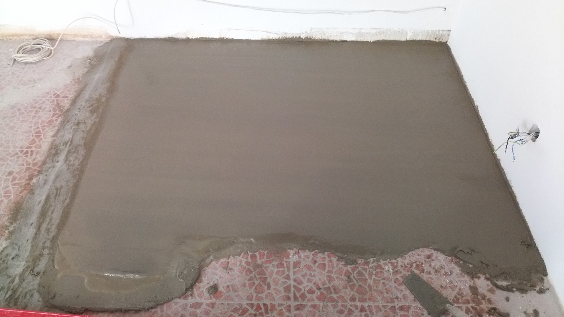 Concreto recém-despejado sobre piso de azulejos. Cimento cinza cobre o centro. O cômodo tem paredes brancas.