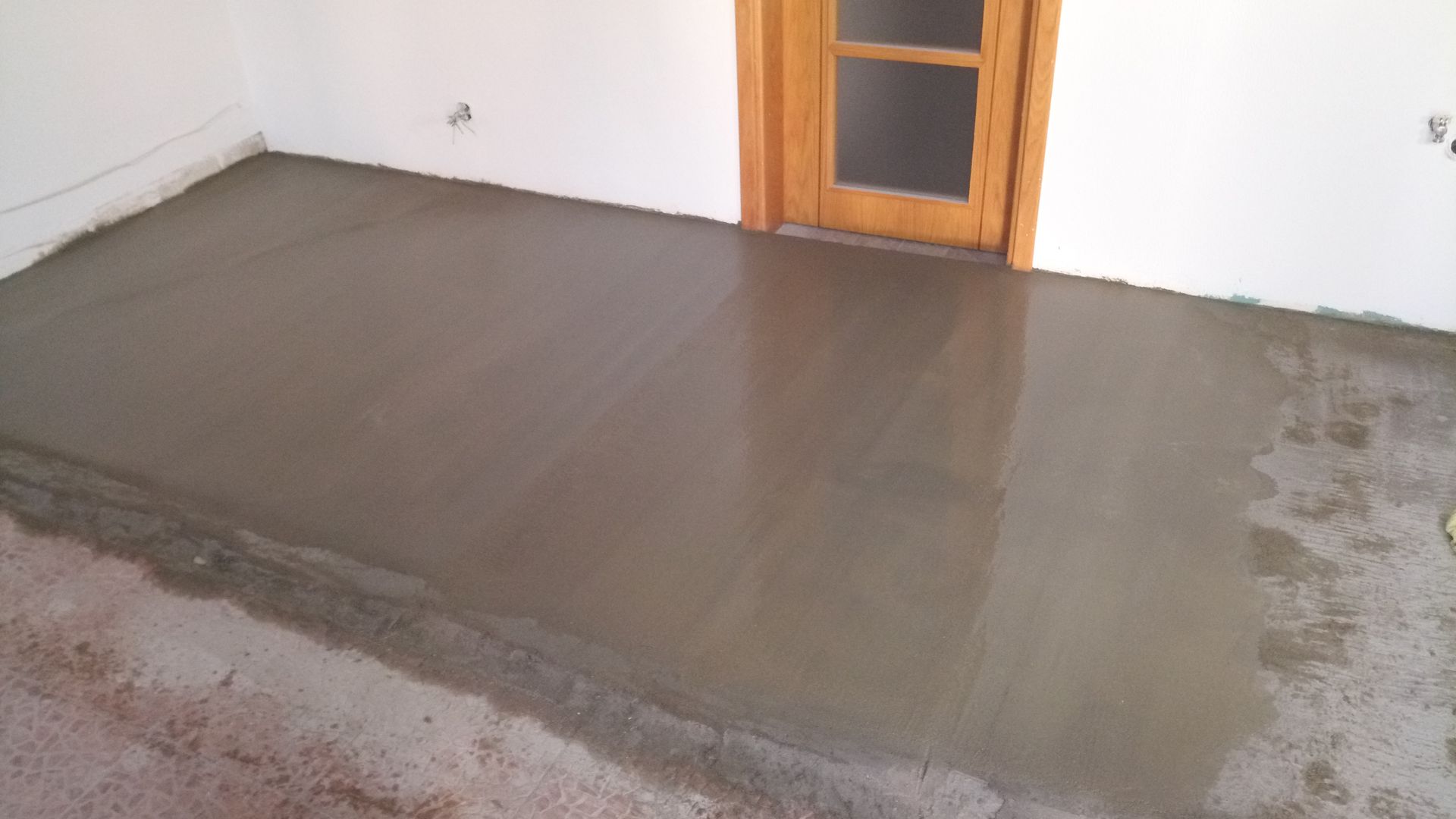 Piso de concreto cinza recém-despejado dentro de um cômodo, próximo a uma porta de madeira e paredes brancas.
