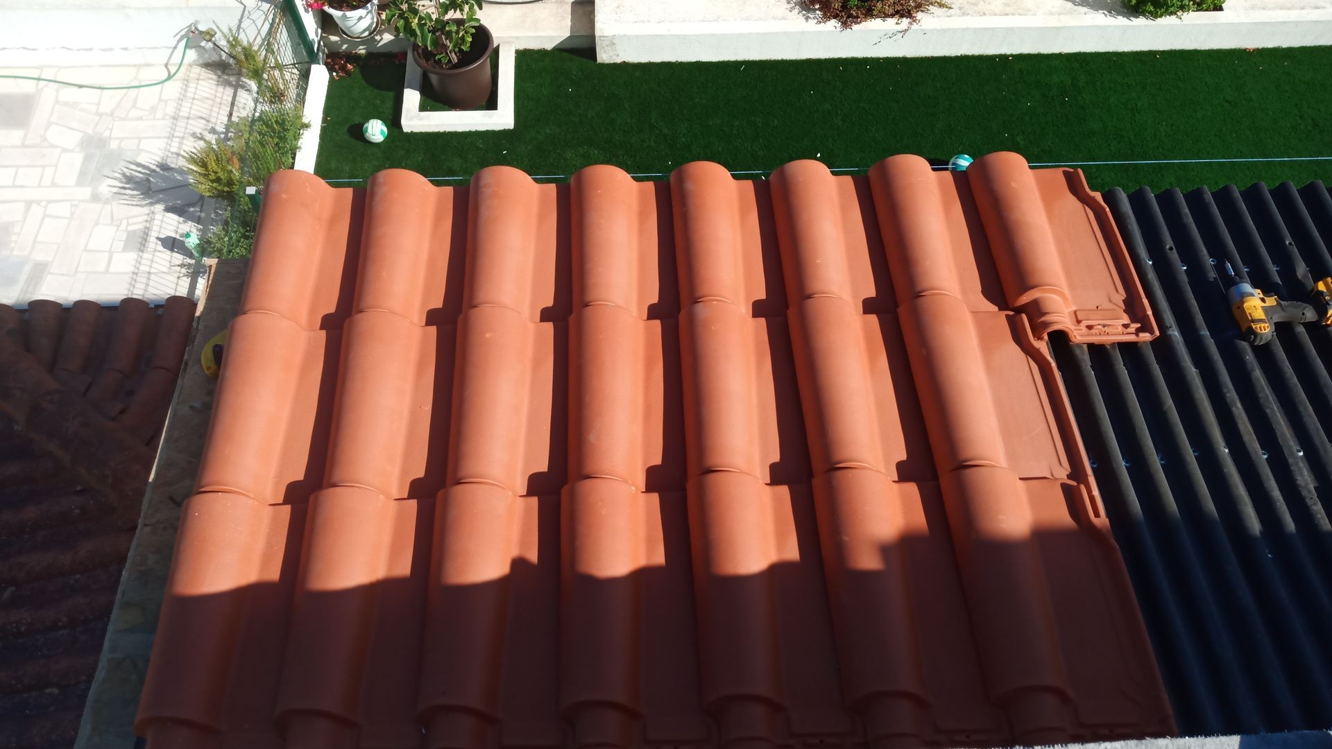 Telhas de terracota vermelhas empilhadas sobre um telhado escuro e ondulado.