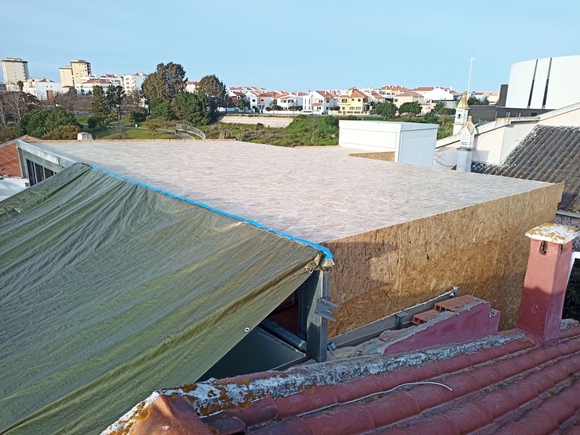 Vista do telhado de um edifício com uma superfície plana e clara e uma lona verde cobrindo uma seção inferior.