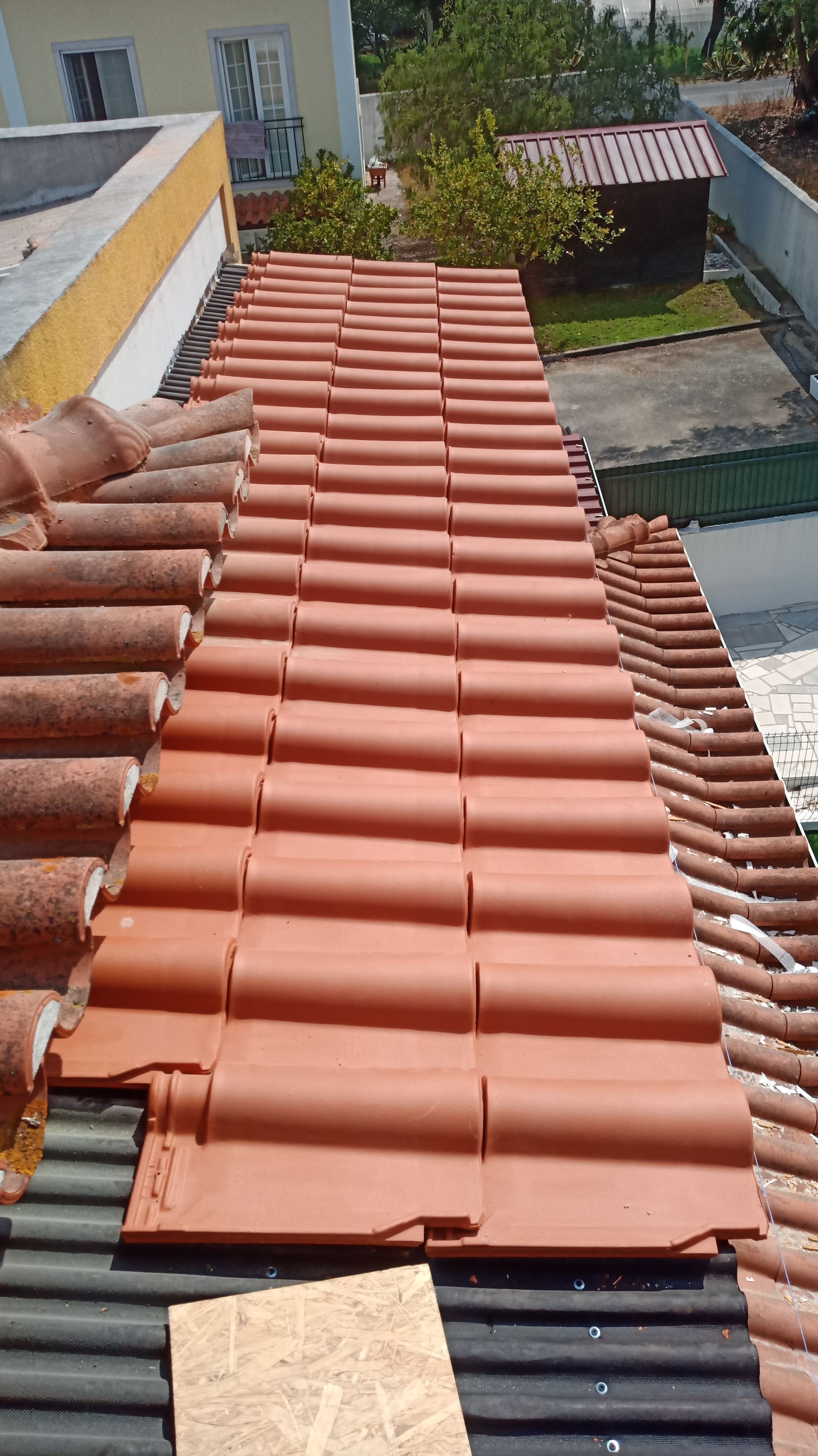 Telhado com telhas de terracota sendo substituídas; tons de cinza e laranja.