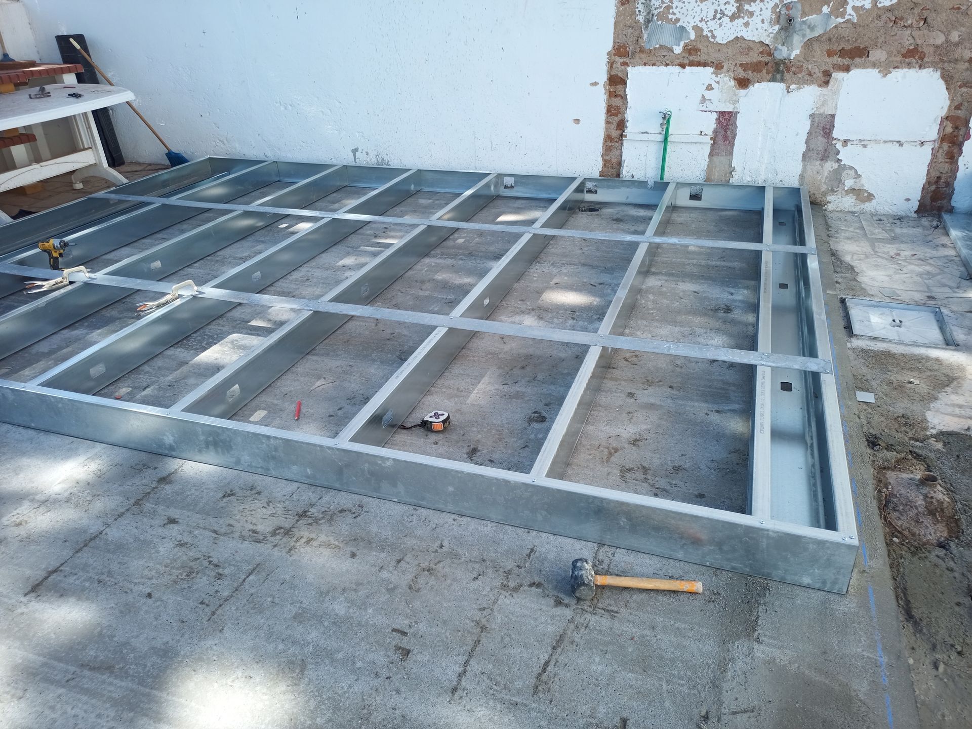 Estrutura metálica em construção sobre uma superfície de concreto. Um martelo está apoiado no concreto.