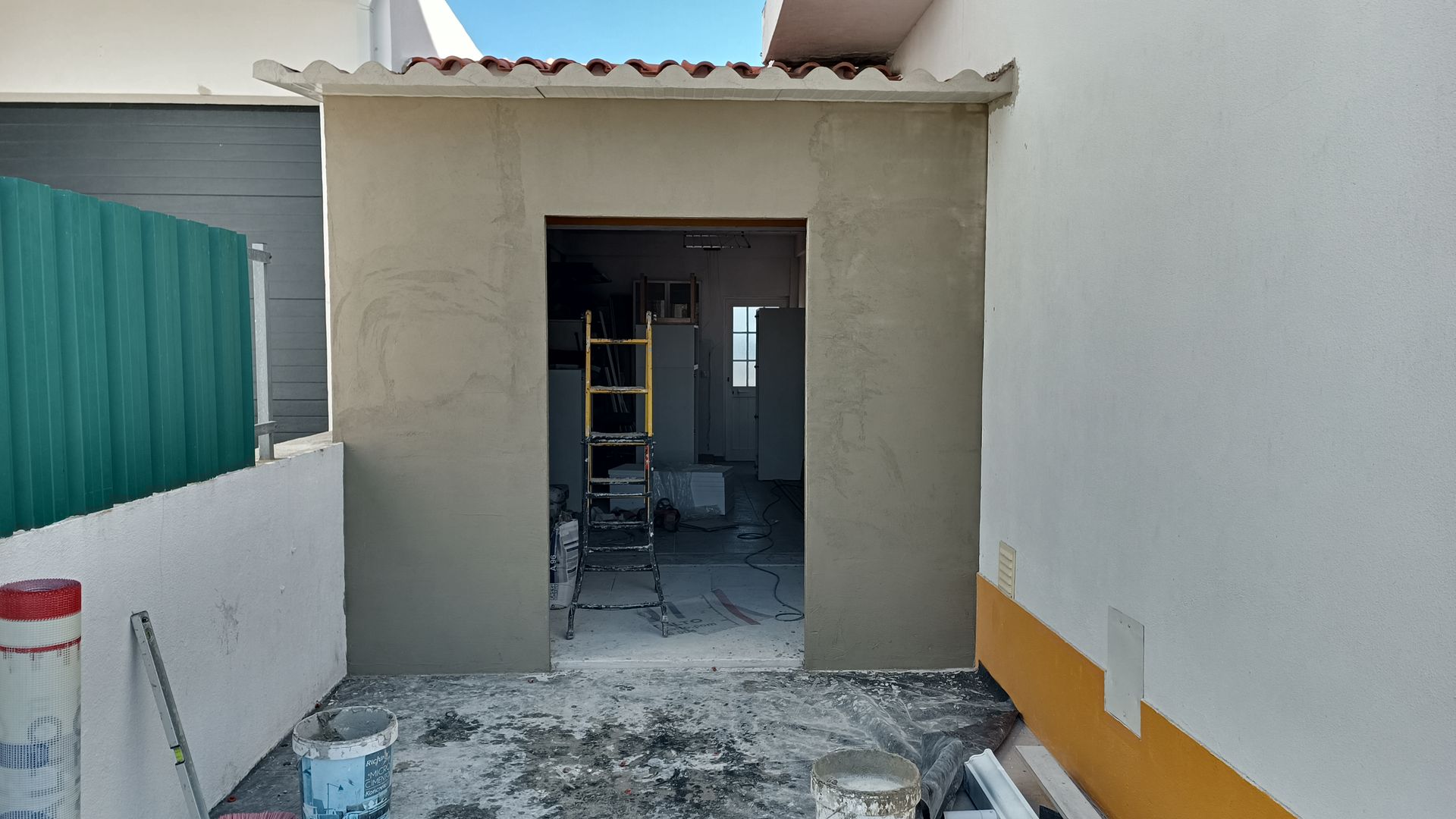 Porta externa em construção, cercada por muros, com parte do telhado.