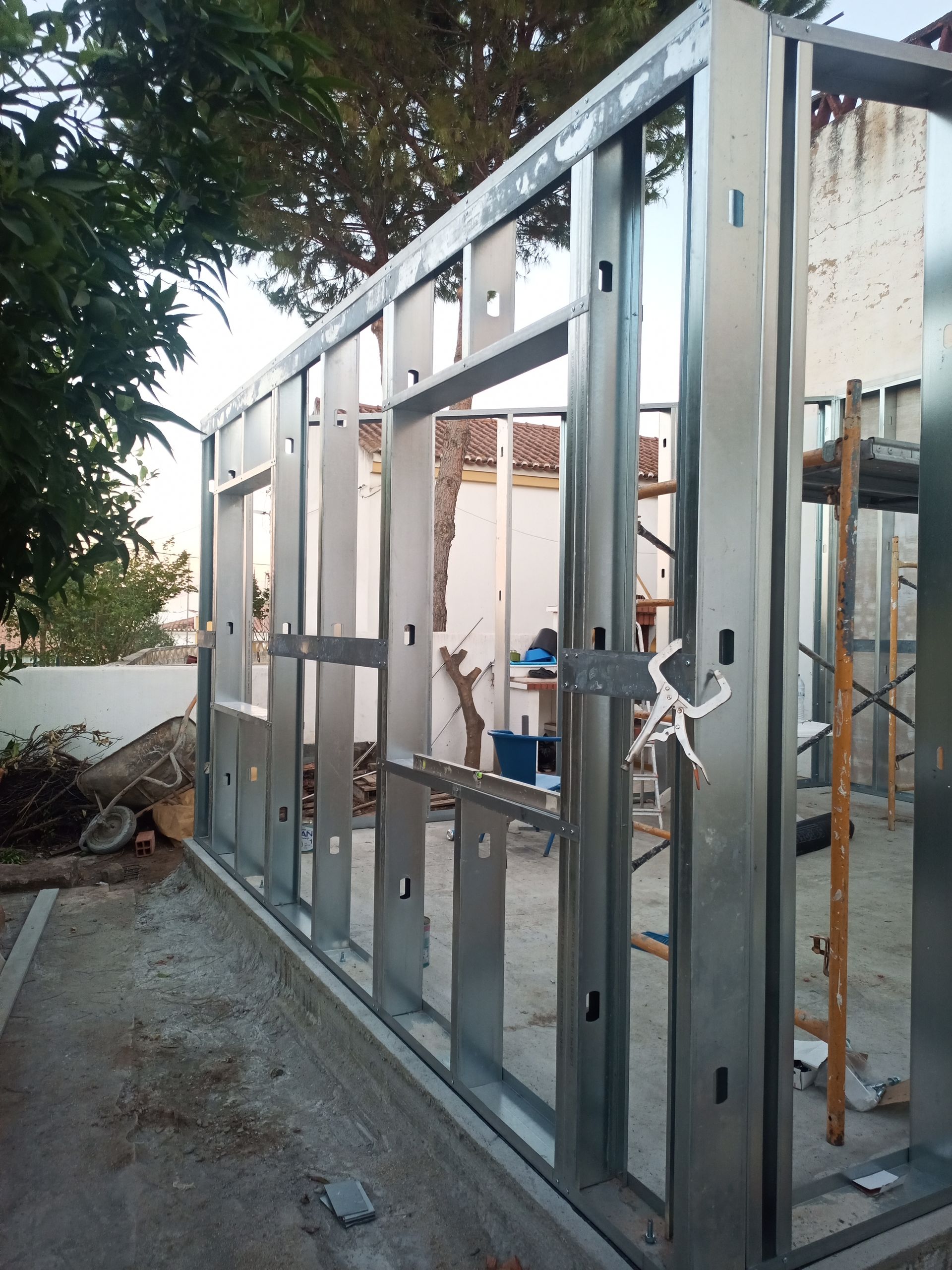 Estrutura metálica para a parede de um edifício, com aberturas para janelas e portas, assentada sobre uma base de concreto.