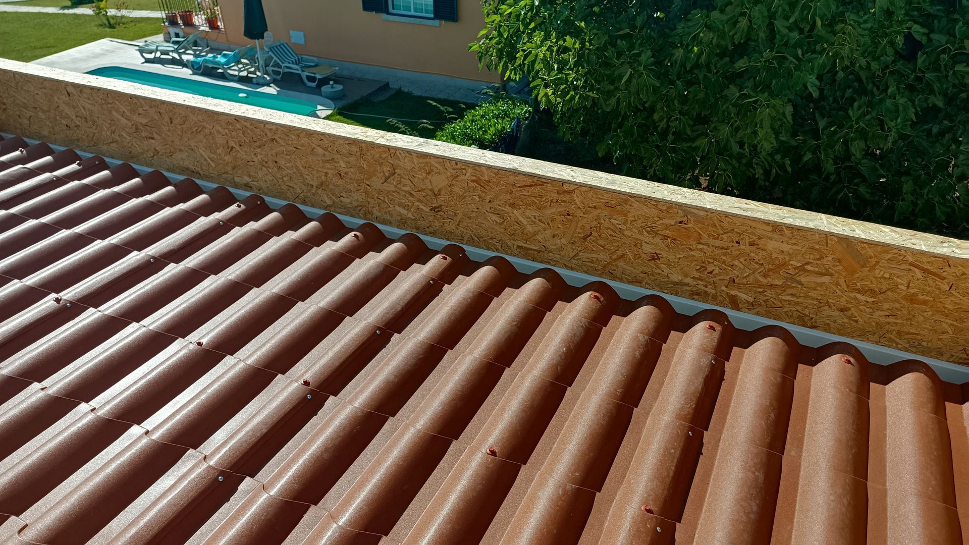 Telhado de zinco vermelho com borda marrom-clara e vista para uma piscina e árvores.